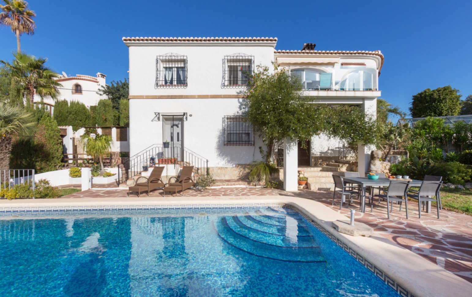 Außenansicht der Villa mit privatem Pool, Natursteinterrasse mit Essbereich und weißer Fassade mit traditionellen schmiedeeisernen Fenstergittern.