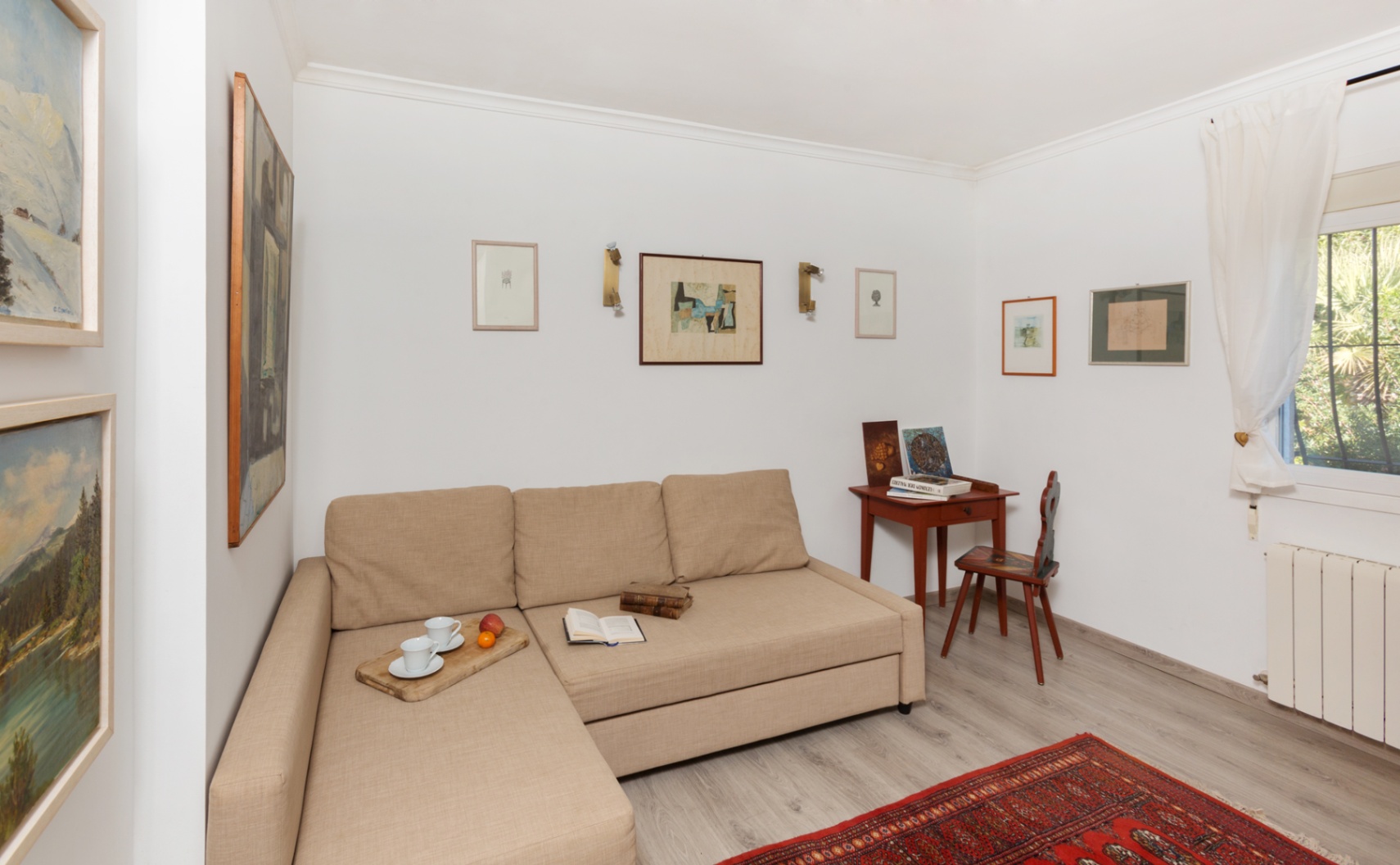 Heller Sitzbereich mit beigem Chaiselongue-Sofa, klassischem Holzschreibtisch und einer Bildergalerie an den weißen Wänden über grauem Laminat.