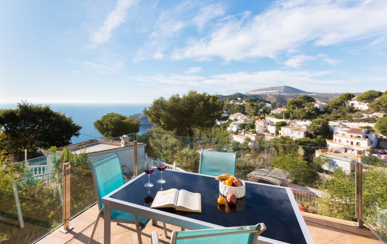 Terrasse mit Glasgeländer, schwarzem Glastisch und Panoramablick auf die Mittelmeerküste und die Hügel von Cumbre del Sol.