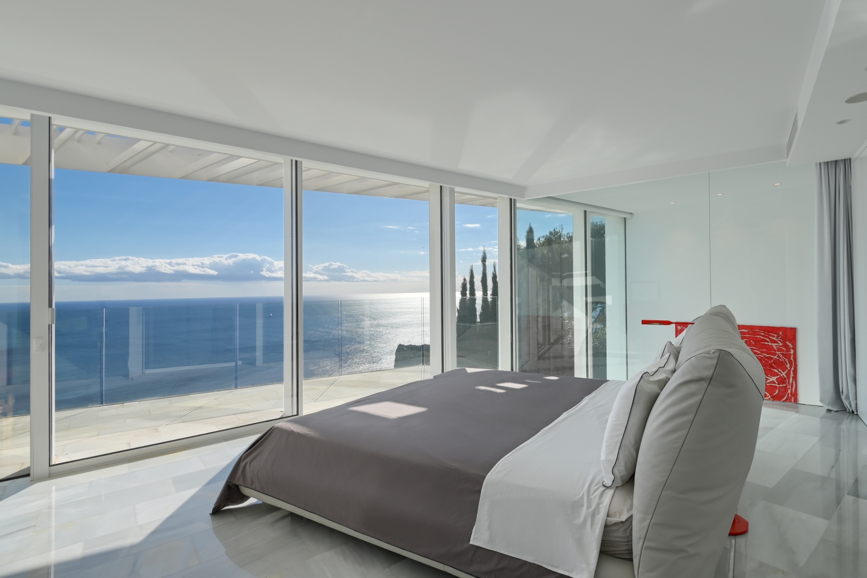 Modernes Hauptschlafzimmer mit bodentiefen Glasfronten, weißem Marmorboden und Panoramablick auf das Mittelmeer von einer privaten Terrasse.