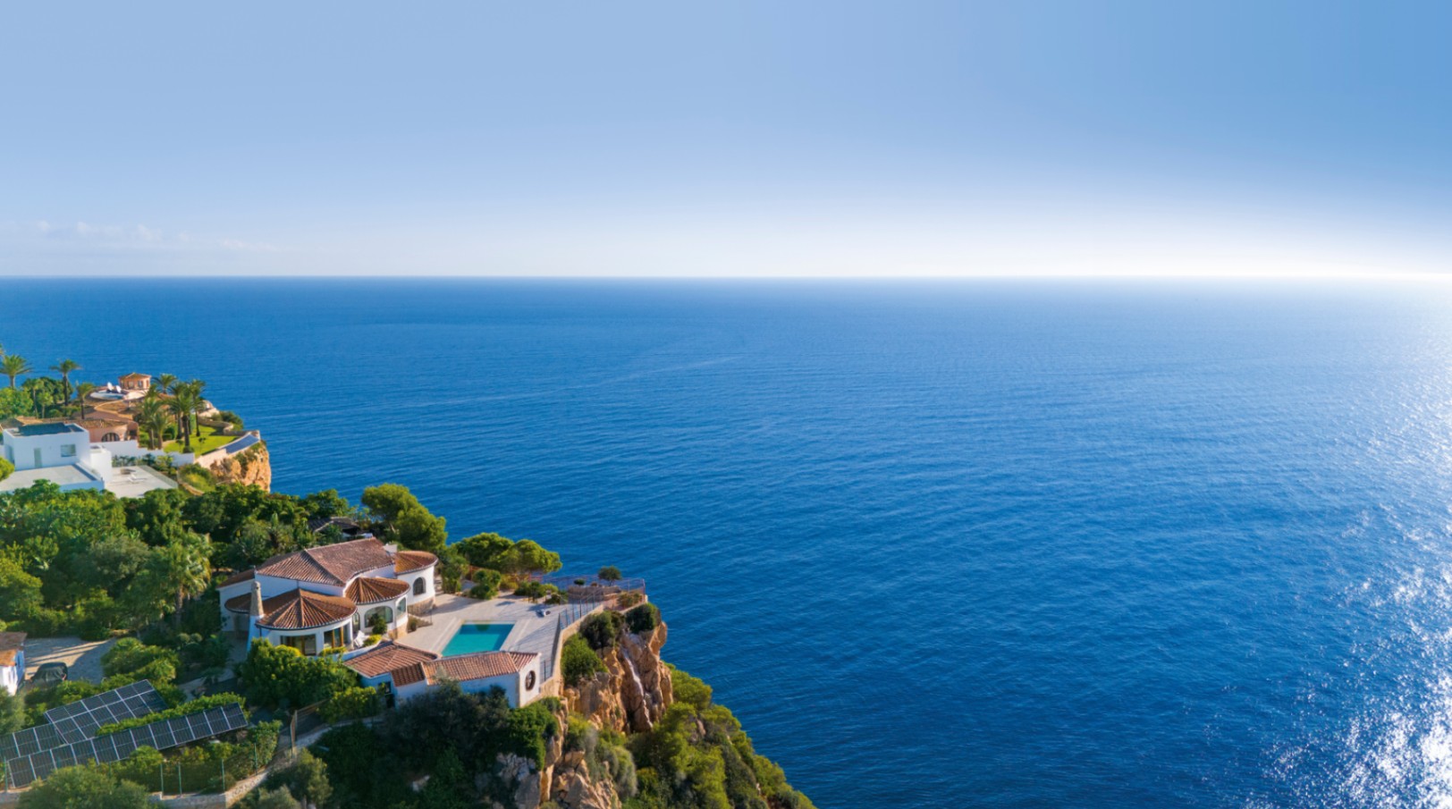 Luftaufnahme einer Villa am Klippenrand mit Terrakottadächern, einer Poolterrasse und weitem Blick über das azurblaue Mittelmeer.