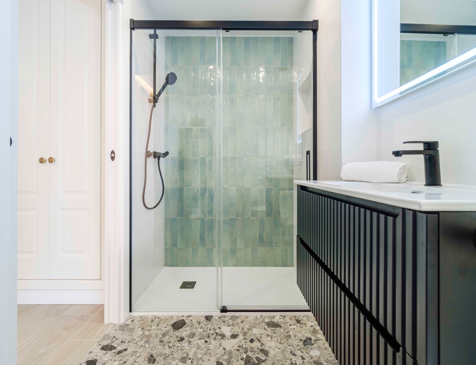 Modernes Badezimmer mit begehbarer Dusche, türkisfarbenen vertikalen Fliesen, schwarzen Armaturen und einem geriffelten Waschtischunterschrank.