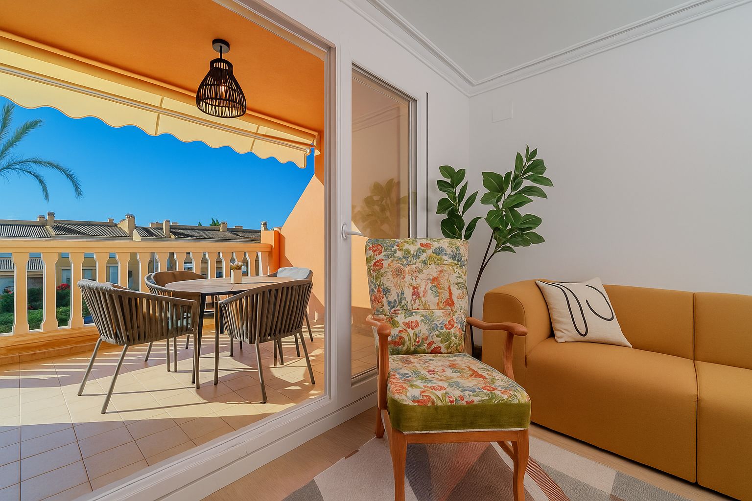 Wohnbereich mit senfgelbem Sofa und geblümtem Sessel, der auf eine private Terrasse mit Essgruppe, gelber Markise und freiem Blick führt.