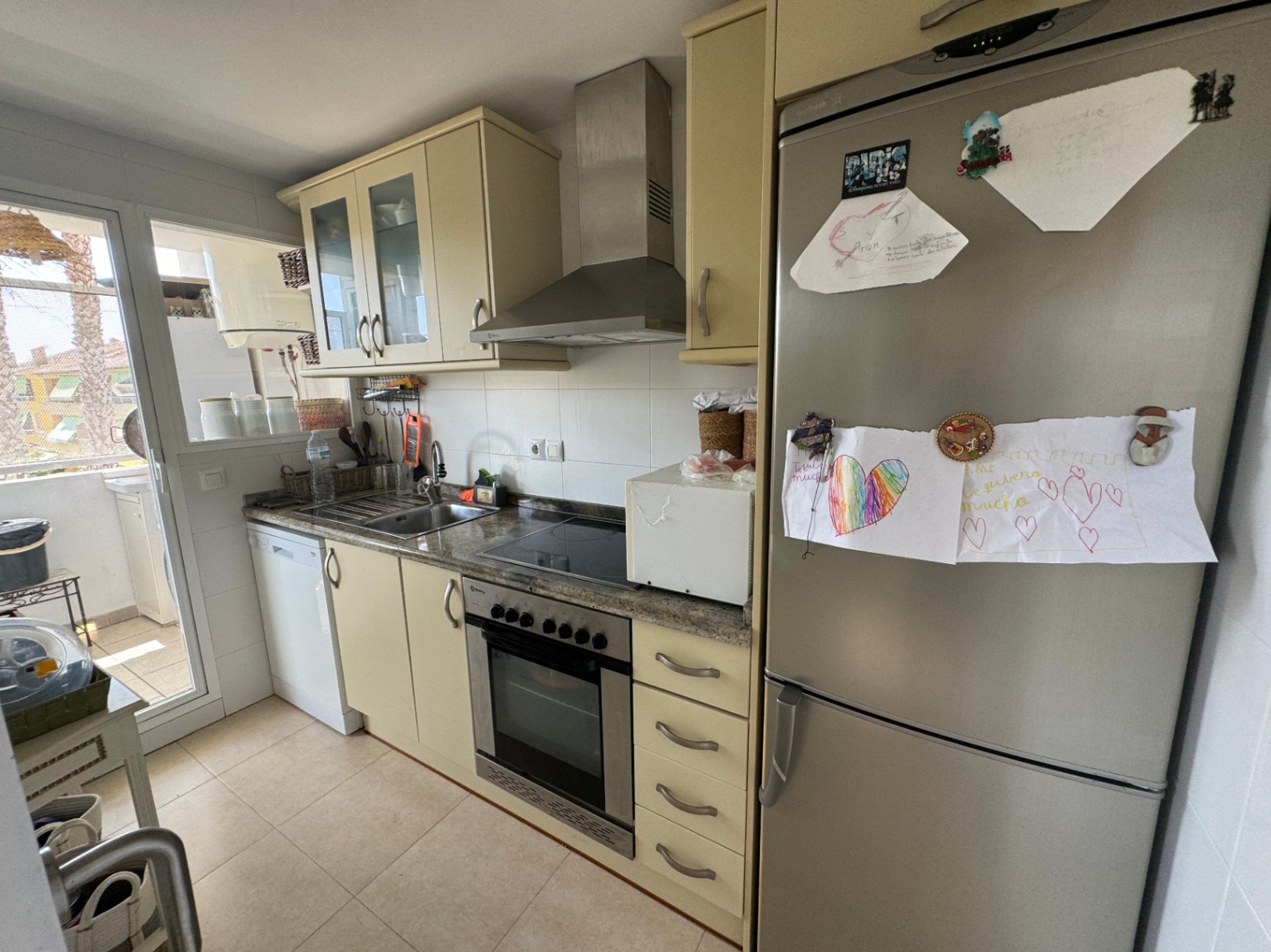 Funktionale Küche mit cremefarbenen Schränken, Granitarbeitsplatte und Edelstahlelektrogeräten. Ausgestattet mit Einbaubackofen, Dunstabzugshaube und Zugang zur Terrasse.