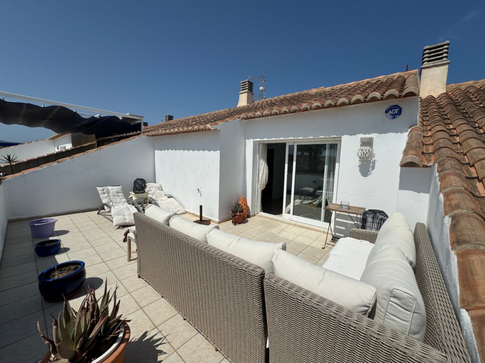 Private Dachterrasse mit Rattansitzgruppe, Fliesenboden und Glasschiebetüren, eingefasst von traditionellen mediterranen Dachziegeln.
