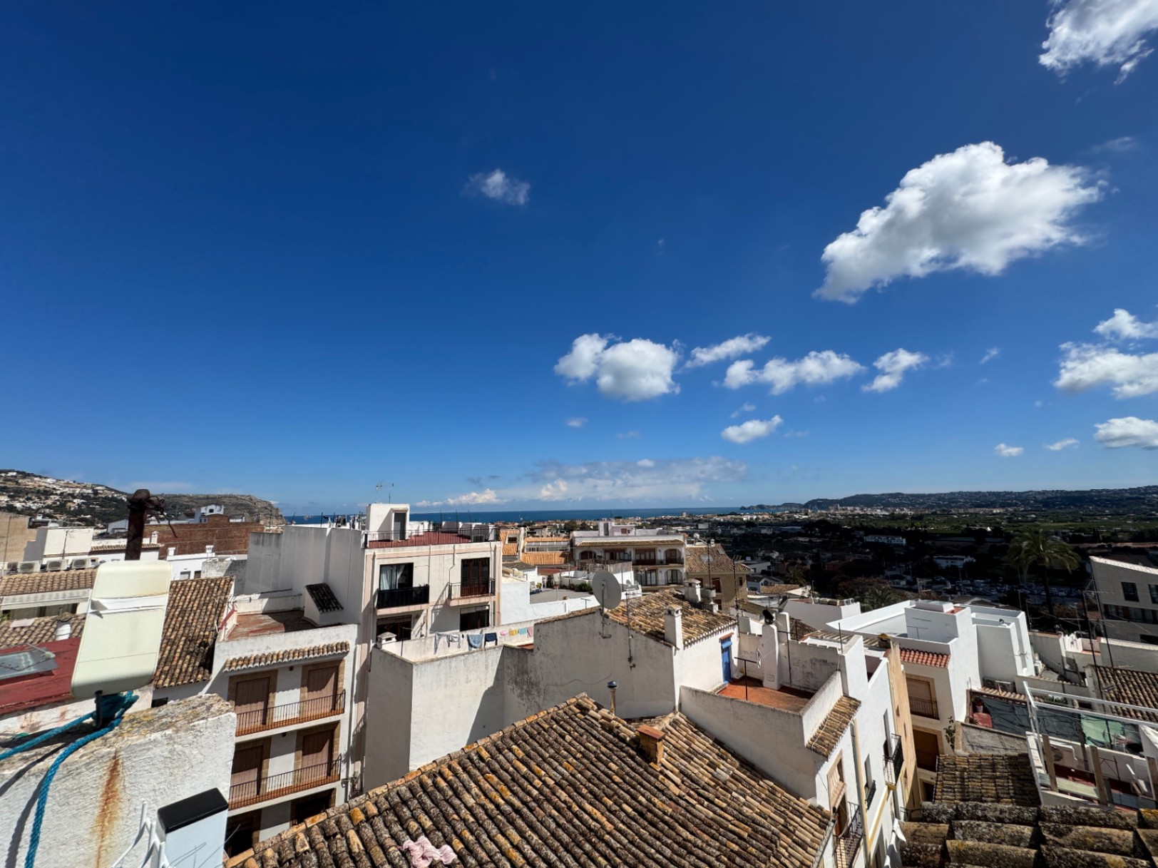 Erhöhter Panoramablick über traditionelle Terrakottadächer und weiße Fassaden bis hin zum Mittelmeer unter strahlend blauem Himmel.
