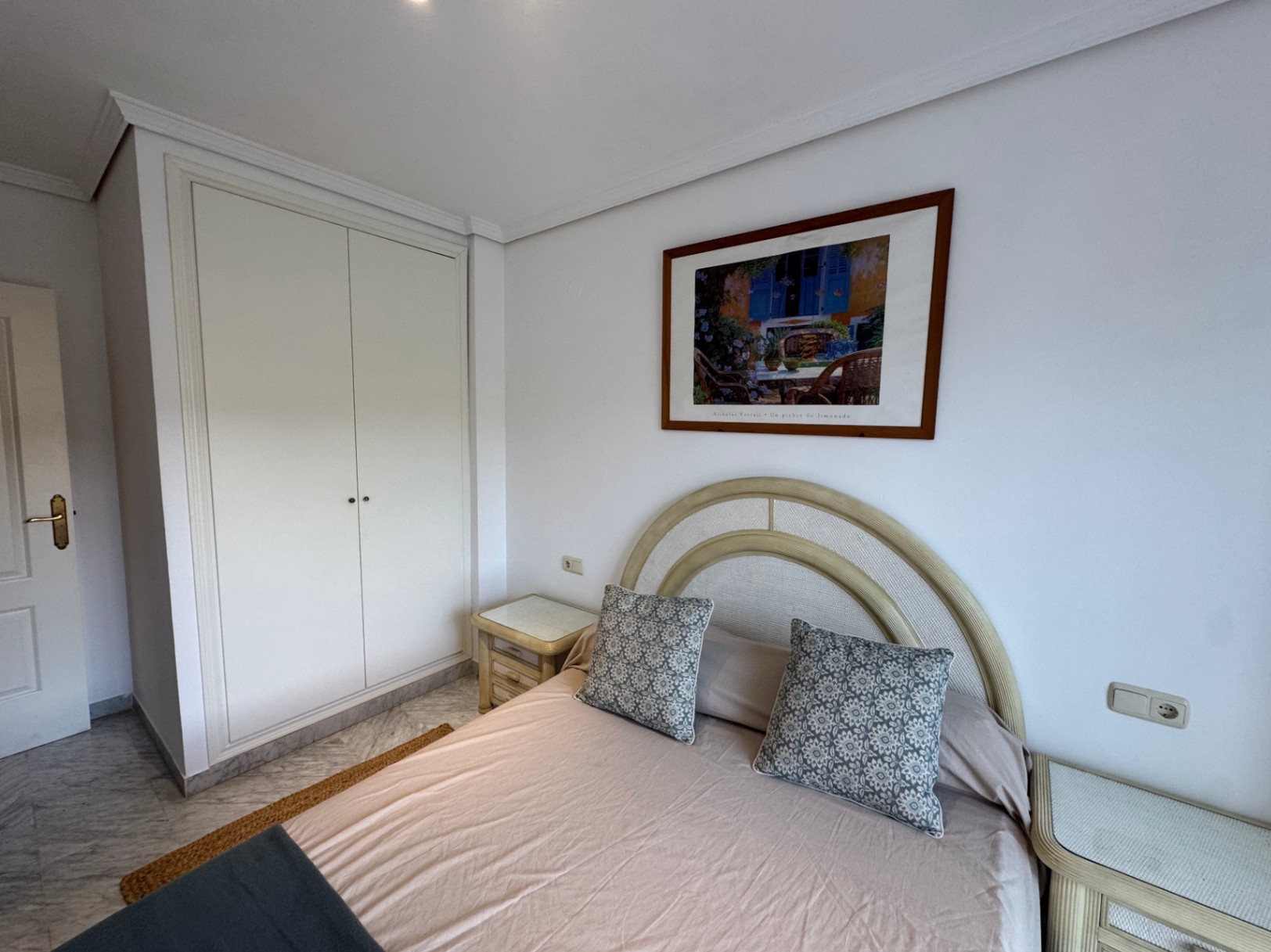 Schlafzimmer mit weißem Einbauschrank, Marmorboden und einem Bett mit geschwungenem Kopfteil sowie passenden Nachttischen.