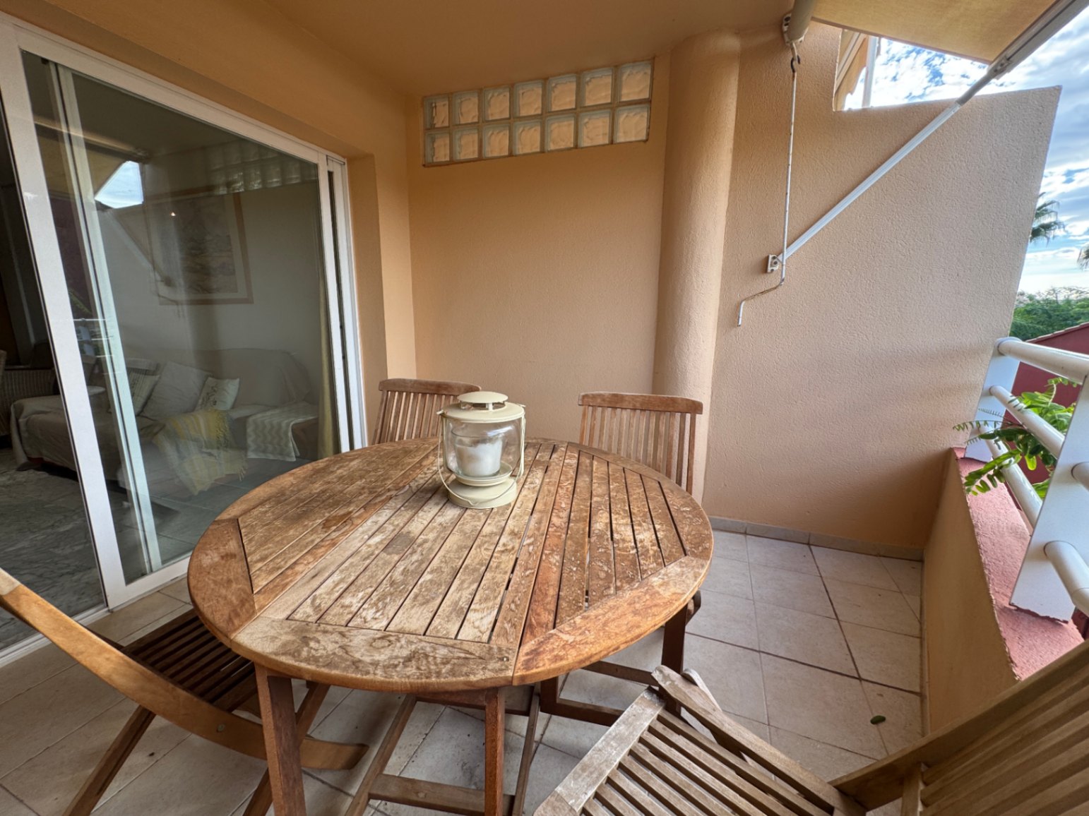 Überdachte Terrasse mit rundem Holztisch-Set und Fliesenboden, zugänglich durch große Glasschiebetüren vom Wohnbereich aus.