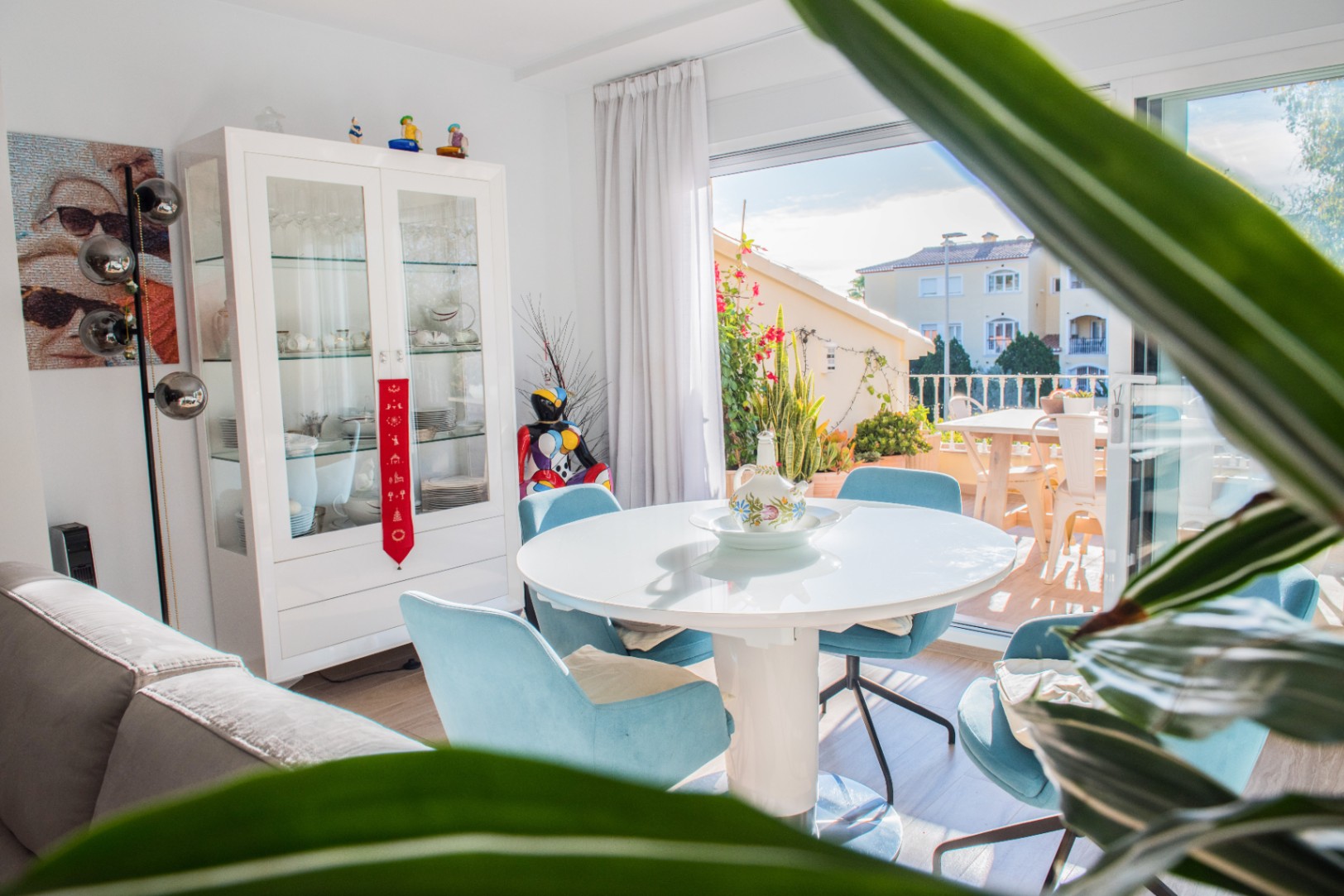 Heller Essbereich mit rundem weißem Tisch, blauen Polsterstühlen und einer Vitrine, mit direktem Zugang zur sonnigen Außenterrasse.