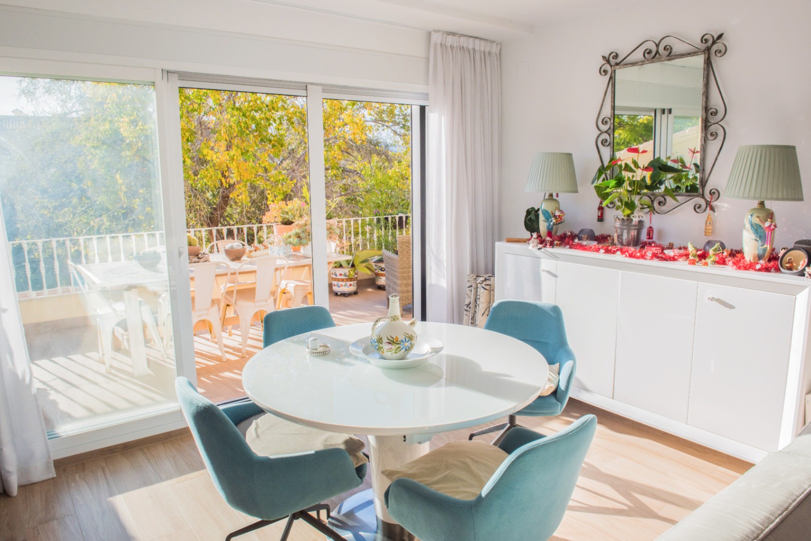 Heller Essbereich mit rundem weißem Tisch und blauen Stühlen, mit direktem Zugang zu einer sonnigen Terrasse durch große Glasschiebetüren.