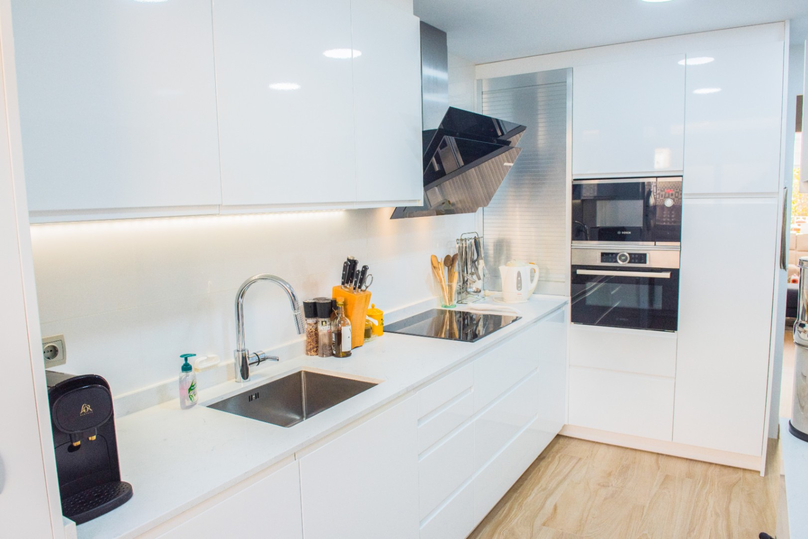 Moderne Küche mit weißen Hochglanzfronten, integrierten Bosch-Geräten und einer weißen Arbeitsplatte mit Induktionskochfeld und schräger Dunstabzugshaube.