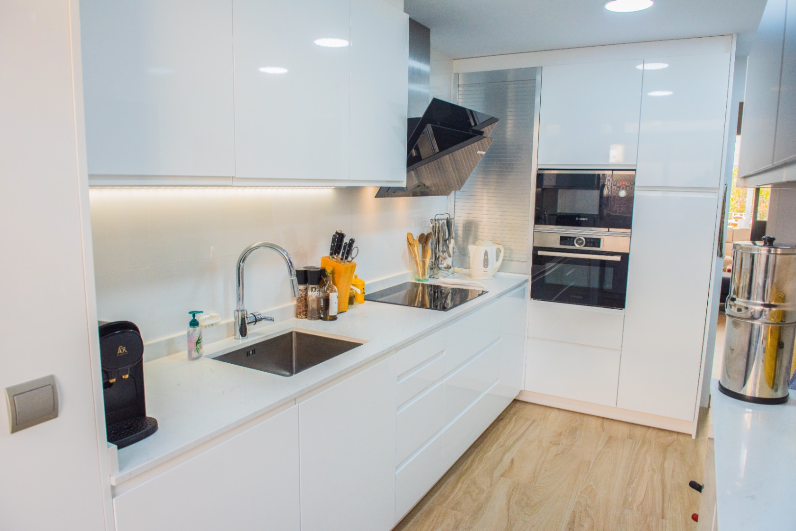 Moderne Küche mit weißen Hochglanzfronten, integrierten Bosch-Geräten und Induktionskochfeld. Ausgestattet mit weißer Quarz-Arbeitsplatte und hellem Holzboden.