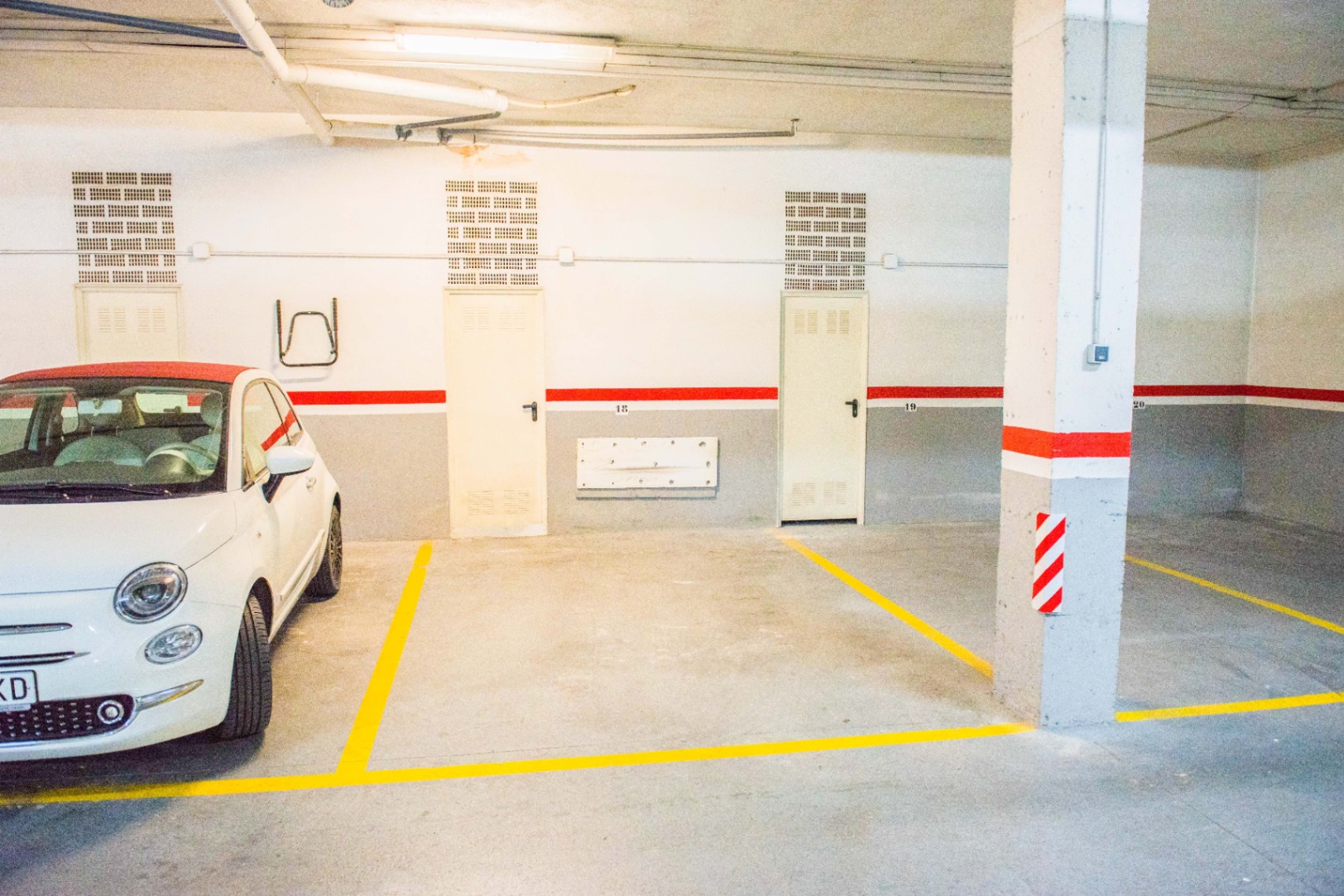 Tiefgaragenplatz mit nummerierten Stellflächen, gelben Markierungslinien und weiß-grauen Wänden mit rotem Akzentstreifen sowie Betonpfeilern.