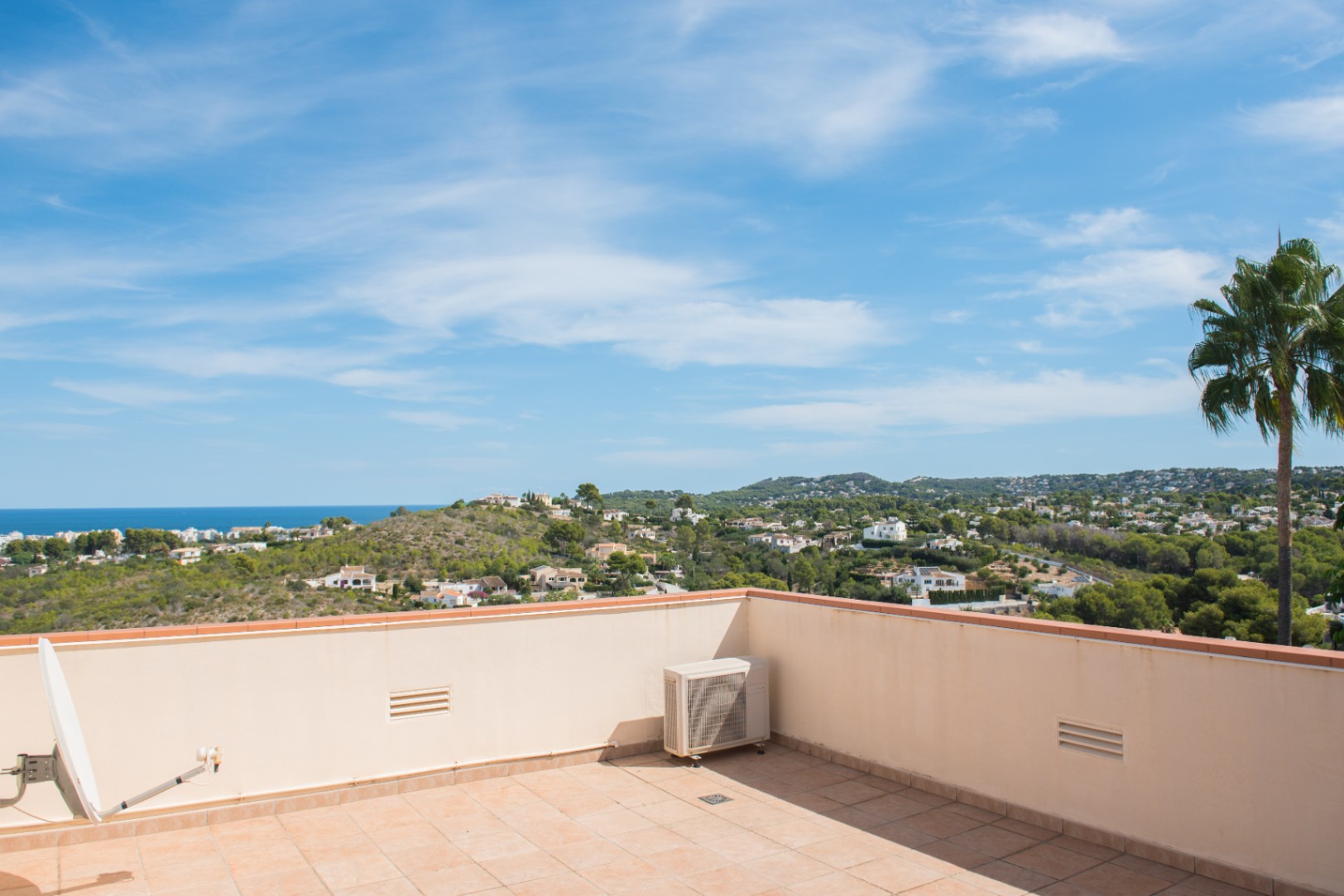 Dachterrasse mit Terrakottafliesen und Panoramablick auf die Mittelmeerküste, bewaldete Hügel und Wohngebiete unter blauem Himmel.
