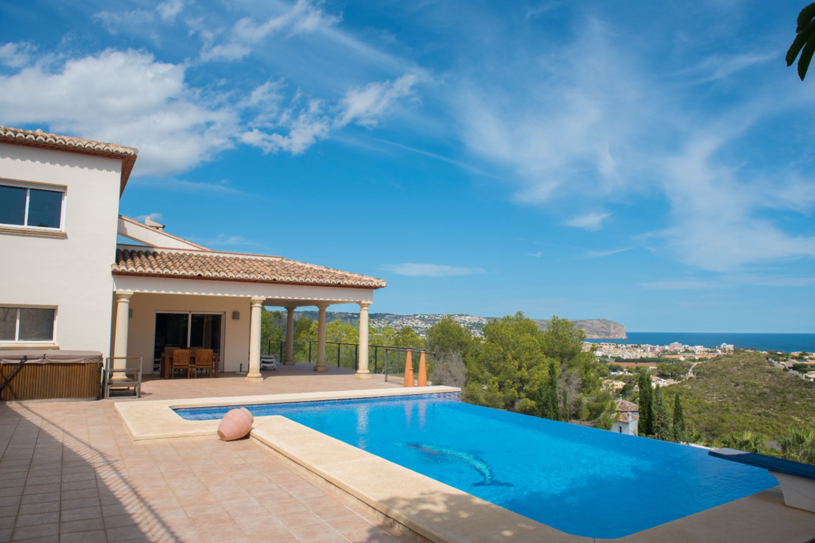 Infinity-Pool mit Delphin-Mosaik und Panoramablick auf das Mittelmeer. Die Villa verfügt über eine überdachte Terrasse mit Steinsäulen und Ziegeldach.