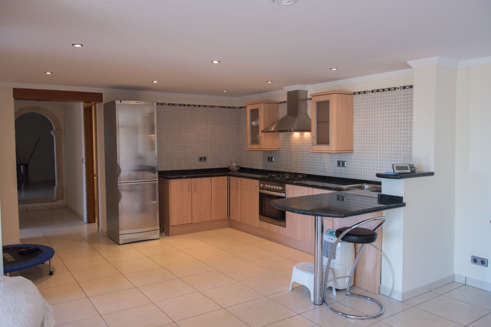 L-Küche mit hellen Holzfronten, dunklen Granitarbeitsplatten und Edelstahlgeräten. Mit Frühstücksbar, Mosaik-Fliesenspiegel und Deckeneinbaustrahlern ausgestattet.