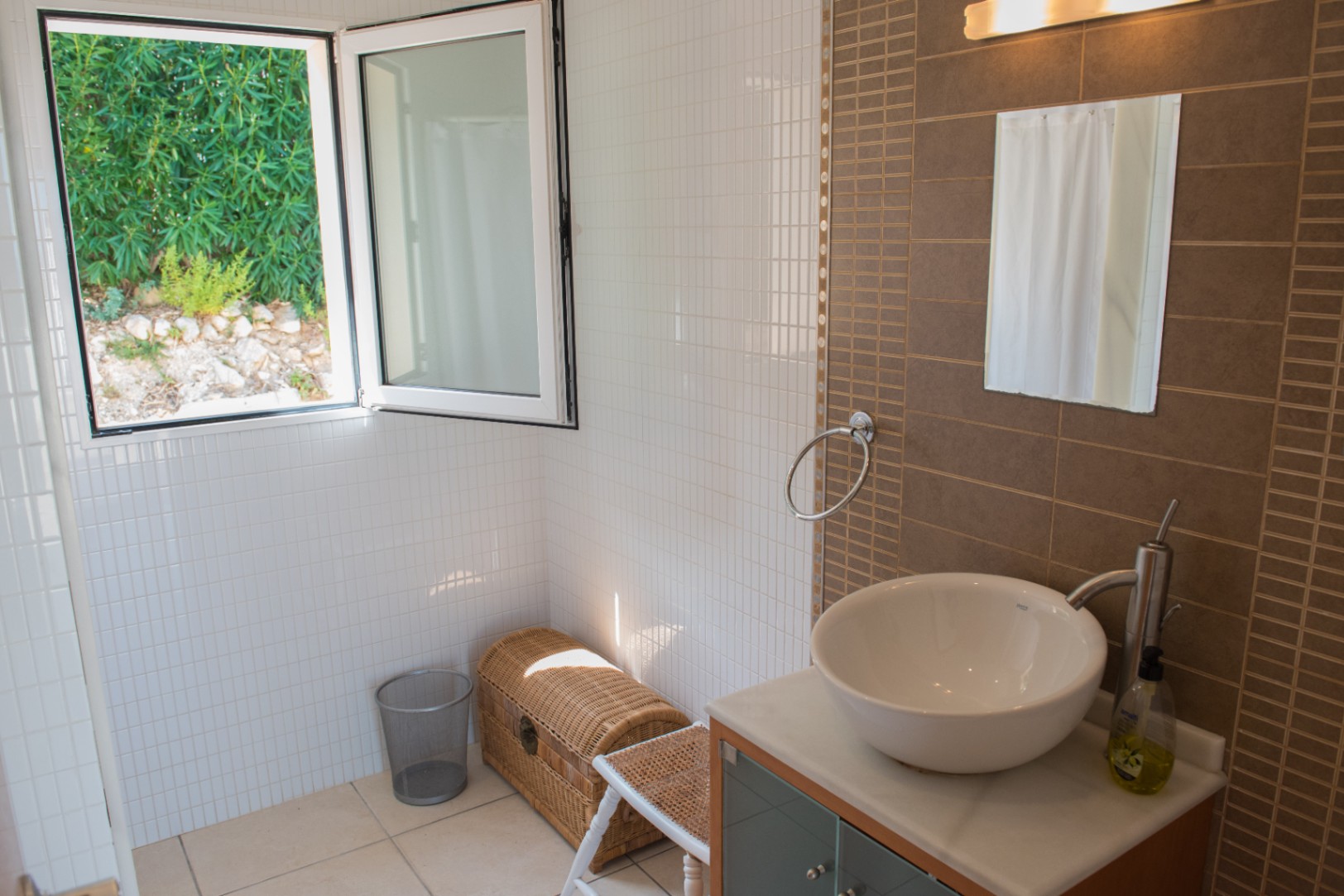 Modernes Badezimmer mit Aufsatzwaschbecken, brauner Akzentwand und offenem Fenster mit Blick auf die grüne Gartenlandschaft.