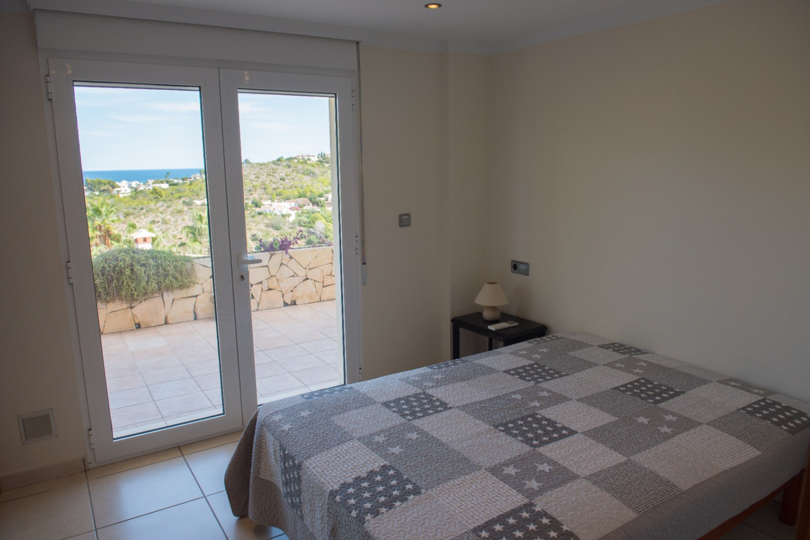 Schlafzimmer mit direktem Zugang zur gefliesten Terrasse durch Glastüren, die einen weiten Blick auf das Meer und die Hügellandschaft bieten.