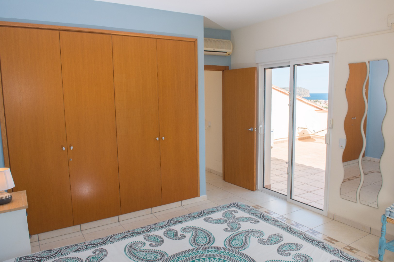 Schlafzimmer mit großem Einbauschrank aus Holz, blauen Akzentwänden und direktem Zugang zu einer privaten Terrasse mit Blick auf das Mittelmeer.