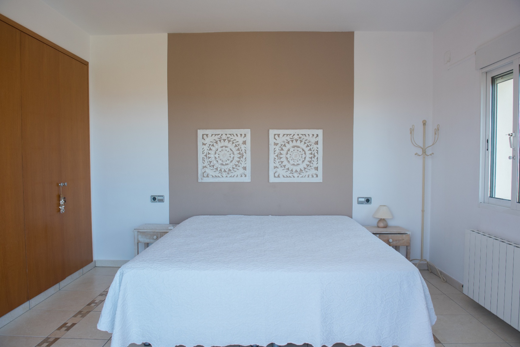 Schlafzimmer mit taupefarbener Akzentwand, geschnitzten Wandpaneelen, Einbauschrank aus Holz und Fliesenboden mit dekorativer Bordüre.