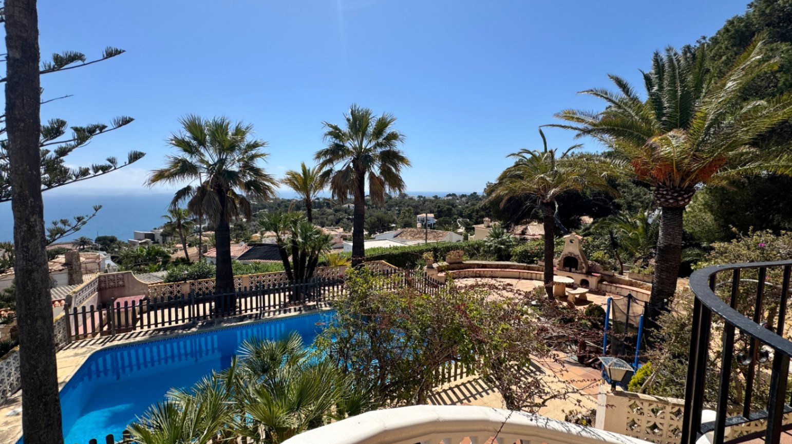 Erhöhter Blick auf einen privaten Pool und eine Steinterrasse mit Außenkamin, umgeben von Palmen und mit weitem Blick auf das Mittelmeer.