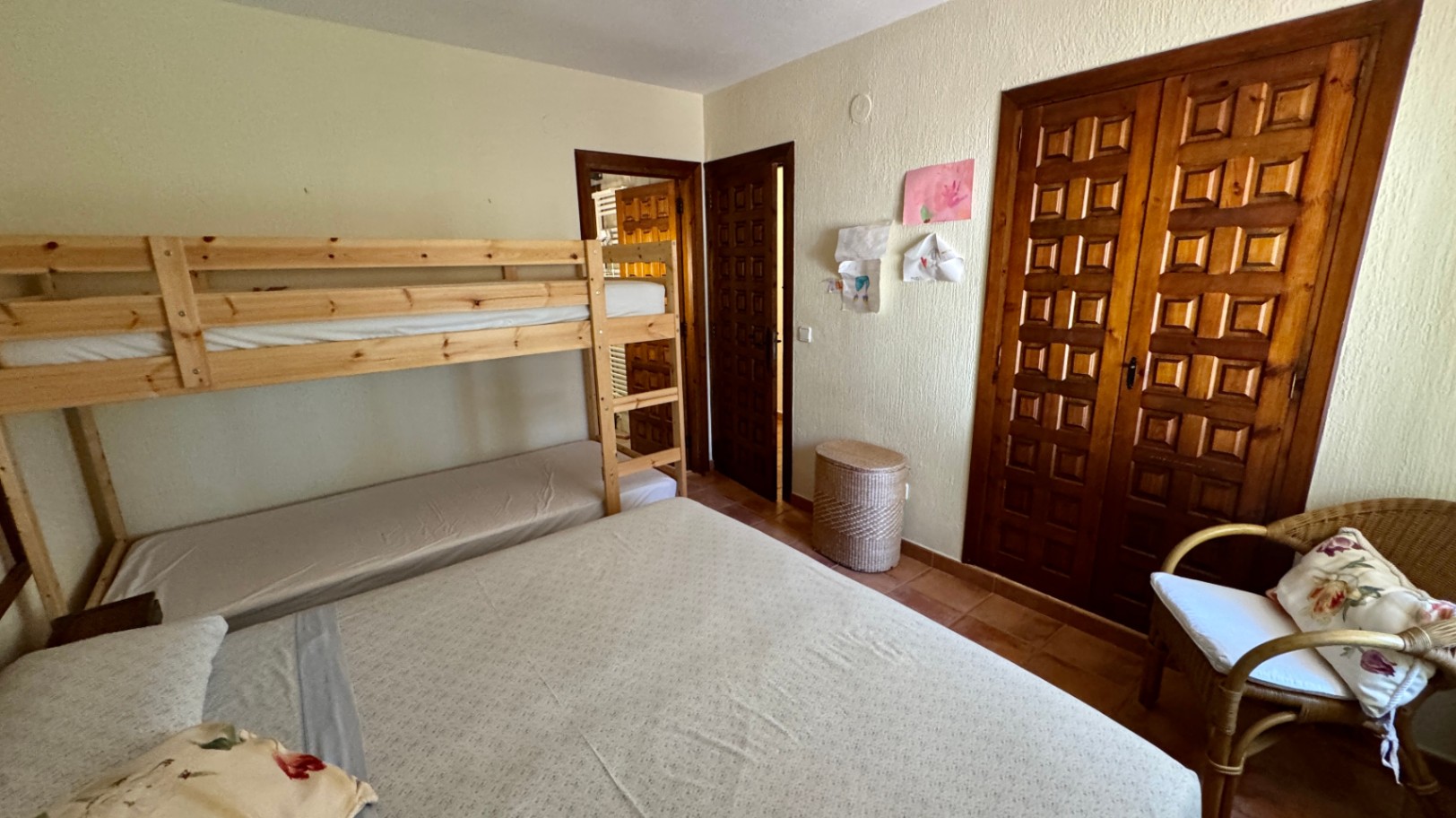 Schlafzimmer mit Etagenbetten aus Kiefernholz, Einbauschrank mit Kassettenfronten und Terrakottafliesen. Ausgestattet mit einem Korbsessel und Strukturputz.