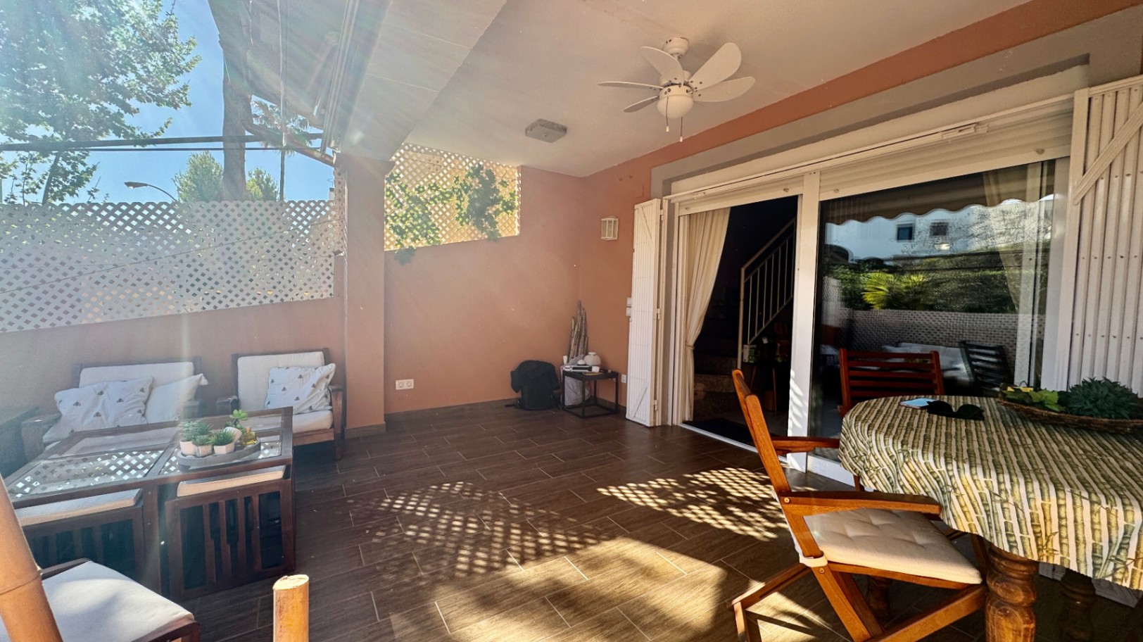 Überdachte Terrasse mit Fliesenboden, Deckenventilator und Glasschiebetüren. Ausgestattet mit einem Loungebereich und Essplatz, geschützt durch Sichtschutzgitter.