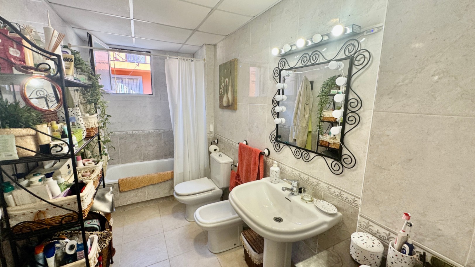 Vollständig gefliestes Badezimmer mit Säulenwaschbecken, einem verzierten Spiegel mit Hollywood-Beleuchtung, Bidet und Badewanne.