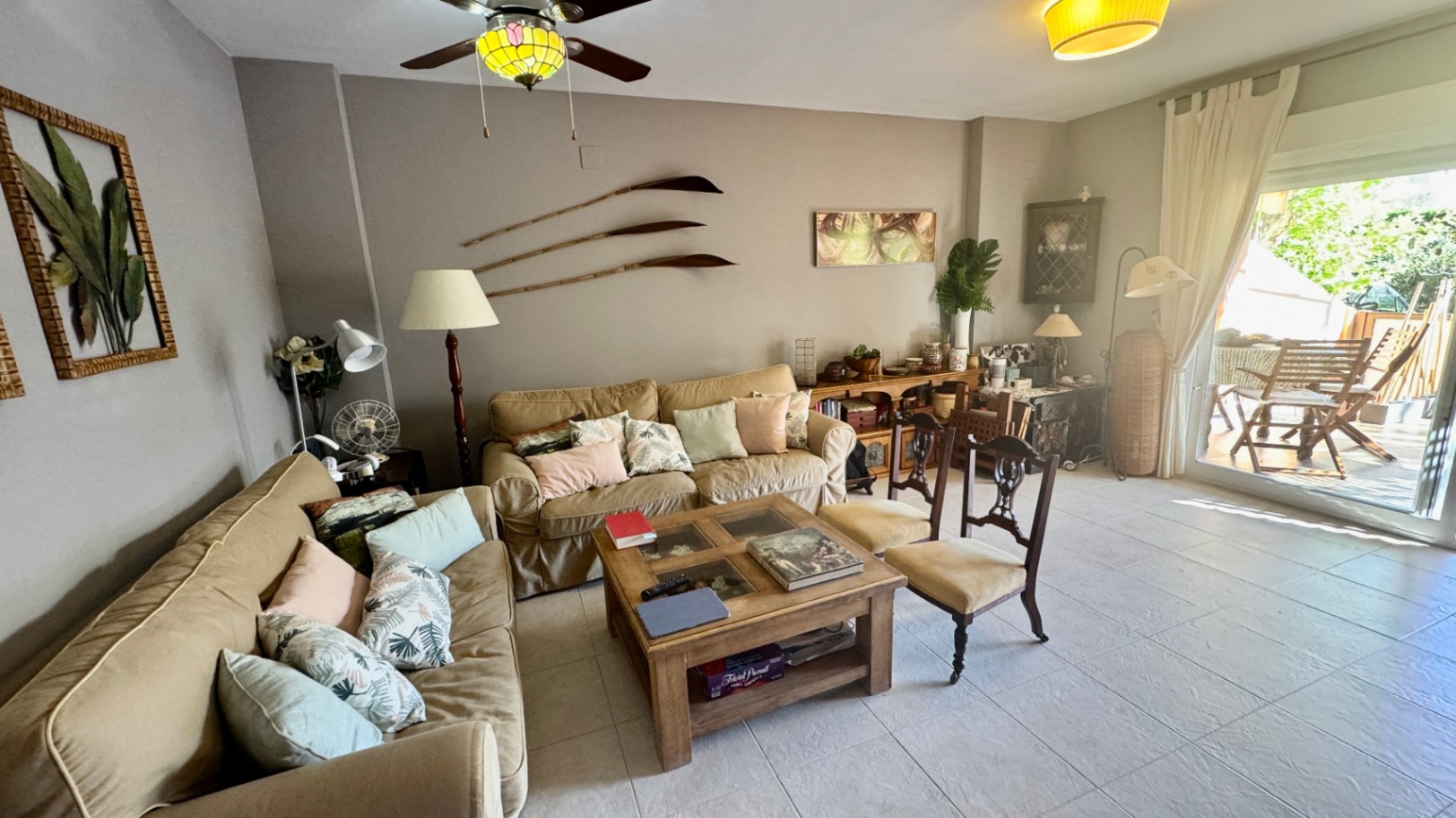 Wohnbereich mit beigen Sofas, einem massiven Holzcouchtisch und direktem Zugang zu einer möblierten Terrasse durch Glastüren.