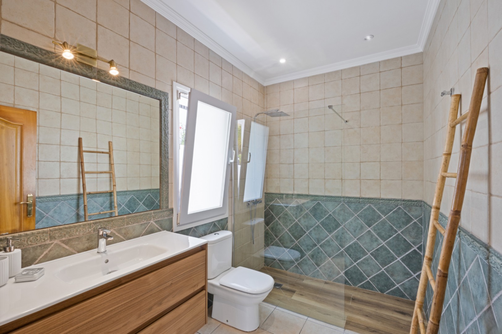 Badezimmer mit begehbarer Dusche in Holzoptik, grünen Rautenfliesen, einem Holzwaschtisch und einer dekorativen Bambusleiter als Handtuchhalter.