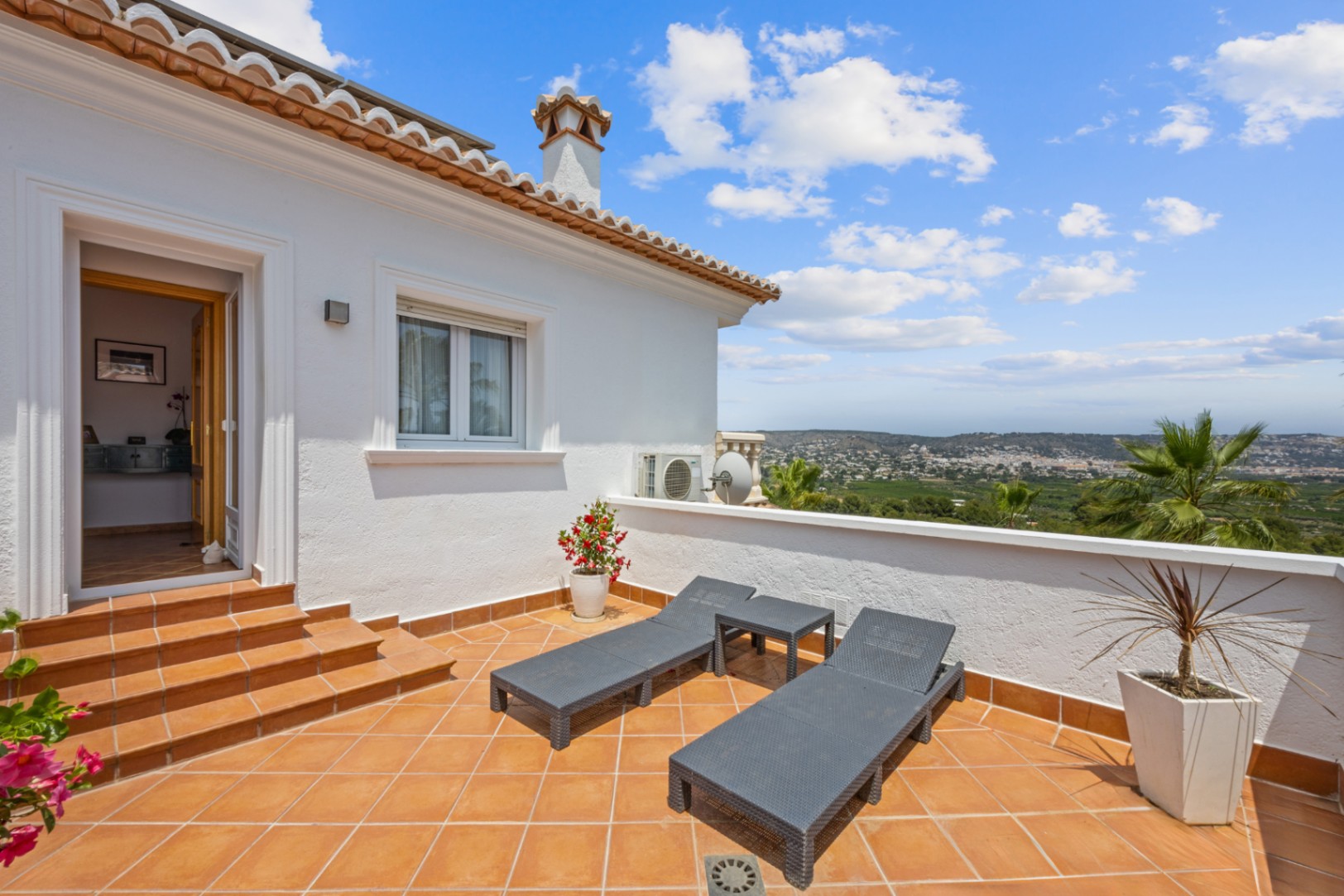 Erhöhte Terrasse mit Terrakotta-Fliesen, grauen Sonnenliegen und Panoramablick auf das Tal. Der Zugang erfolgt über geflieste Stufen vom Innenbereich aus.