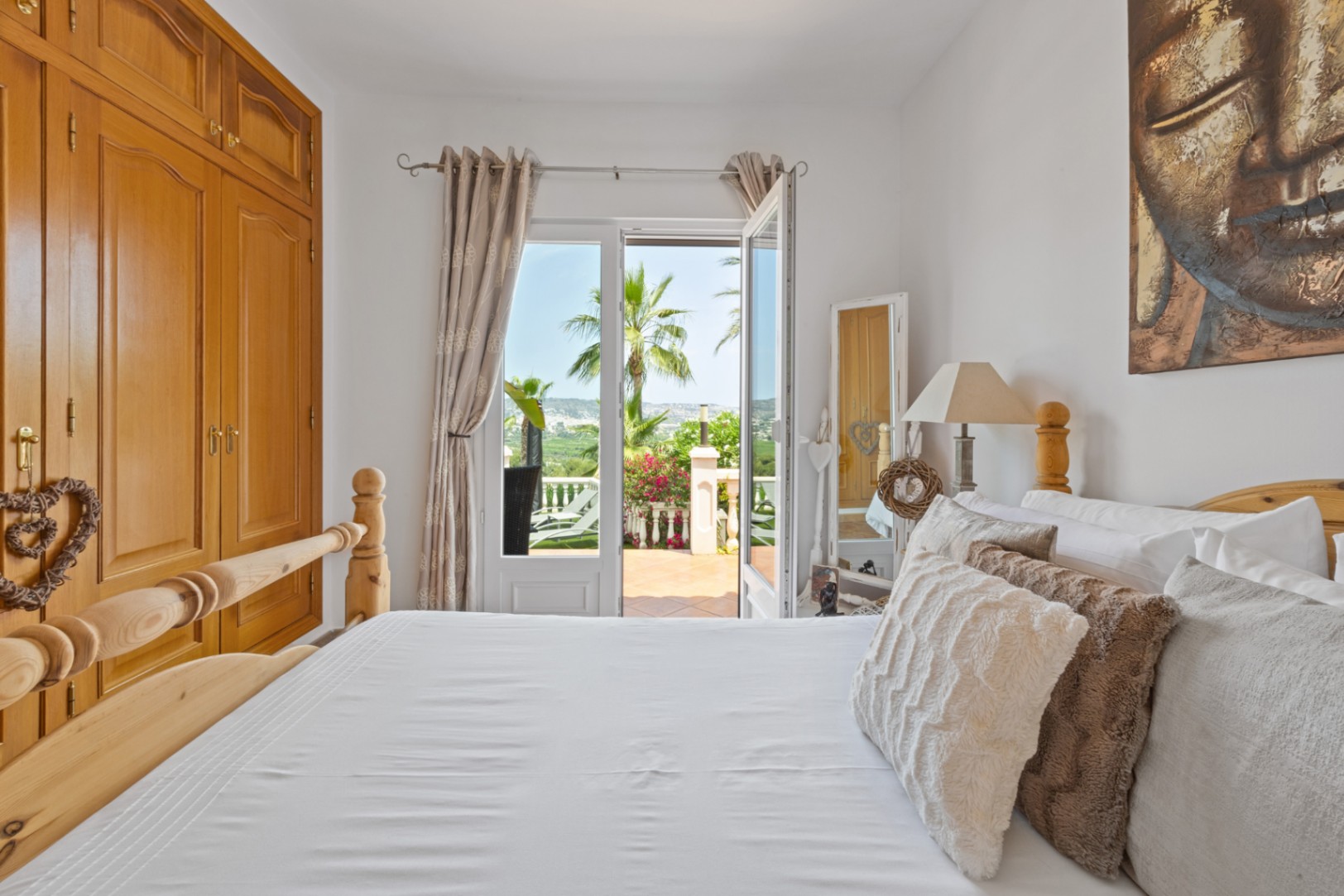 Helles Schlafzimmer mit Einbauschrank aus Holz und Fenstertüren, die auf eine Terrasse mit Blick auf Palmen und die Landschaft führen.