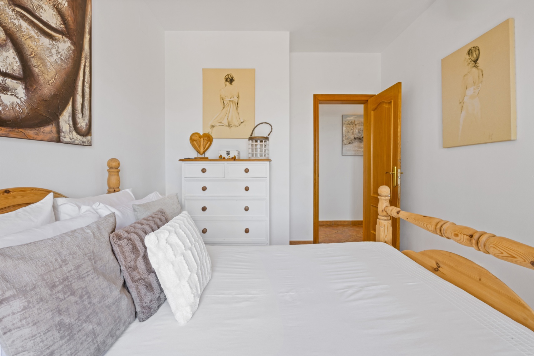 Helles Schlafzimmer mit Massivholz-Bettgestell, weißer Kommode mit Naturholz-Details und dekorativer Wandkunst, einschließlich eines großen Buddha-Leinwandbildes.