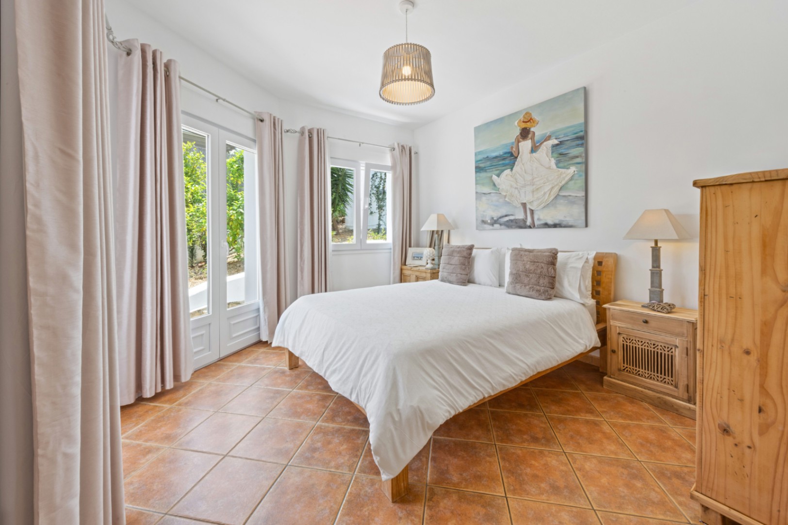 Helles Schlafzimmer mit Terrakotta-Fliesenboden, Holzmöbeln und Glastüren, die viel natürliches Licht hereinlassen und Zugang zum Garten bieten.
