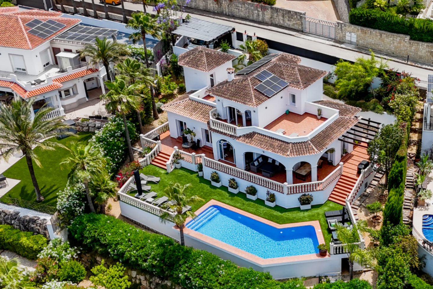 Luftaufnahme einer mediterranen Villa mit geometrischem Pool, Solarmodulen und mehrstufigen Terrakotta-Terrassen mit klassischen weißen Balustraden.
