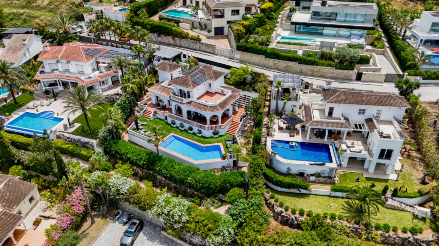 Luftaufnahme luxuriöser mediterraner Villen mit privaten Pools, Terrakottadächern, Sonnenkollektoren und gepflegten Gärten in Hanglage.