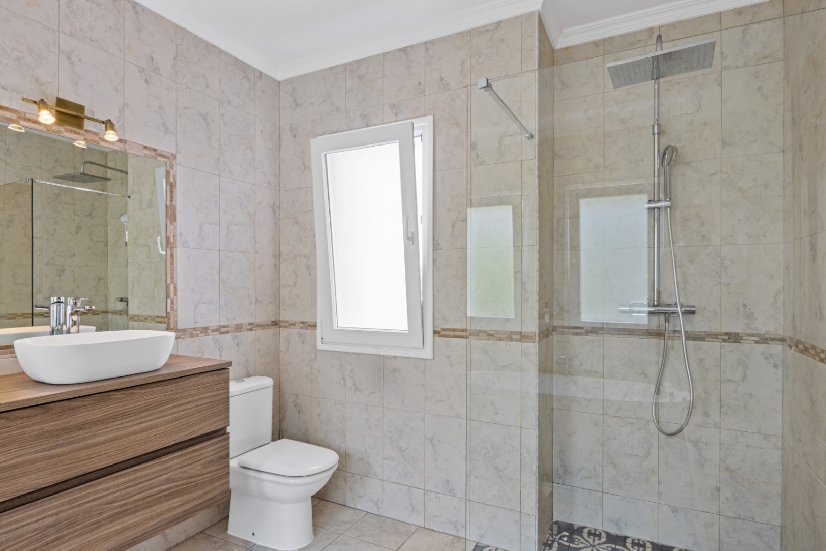 Modernes Badezimmer mit begehbarer Dusche, Glastrennwand, schwebendem Holzwaschtisch mit Aufsatzbecken und beigen Fliesen in Marmoroptik mit Tageslicht.