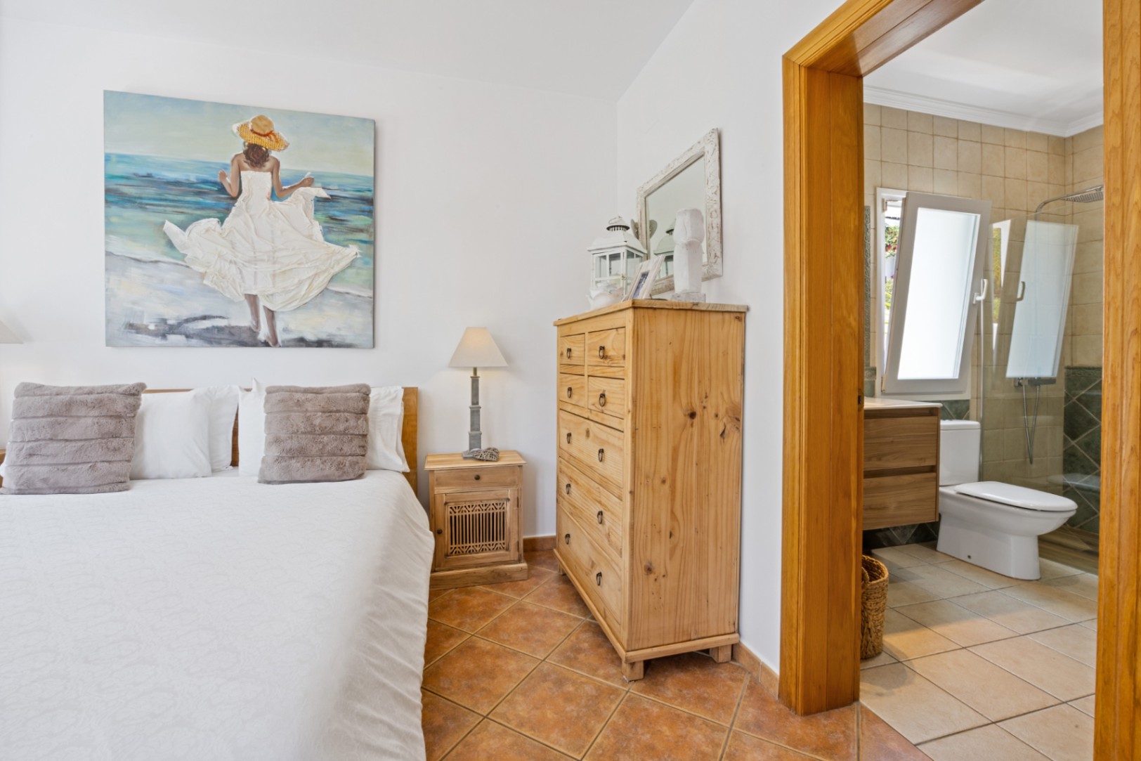 Schlafzimmer mit Terrakottaboden und rustikalen Holzmöbeln, inklusive angrenzendem Badezimmer mit ebenerdiger Dusche und Glaswand.