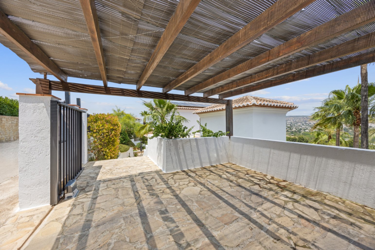 Überdachter Parkplatz mit Holzpergola und Schilfrohrmatten, Naturbruchsteinboden und weitem Blick über die umliegende Hügellandschaft.