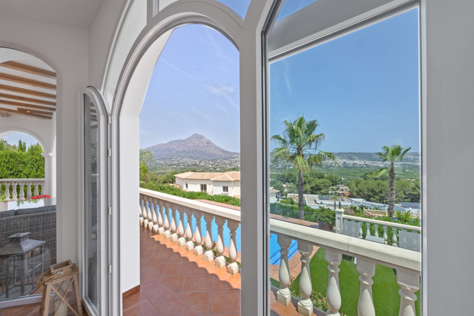 Weiße Rundbogenfenster rahmen den Panoramablick auf die Berge und das Tal ein, mit Blick auf eine Terrakotta-Terrasse und den privaten Poolbereich.