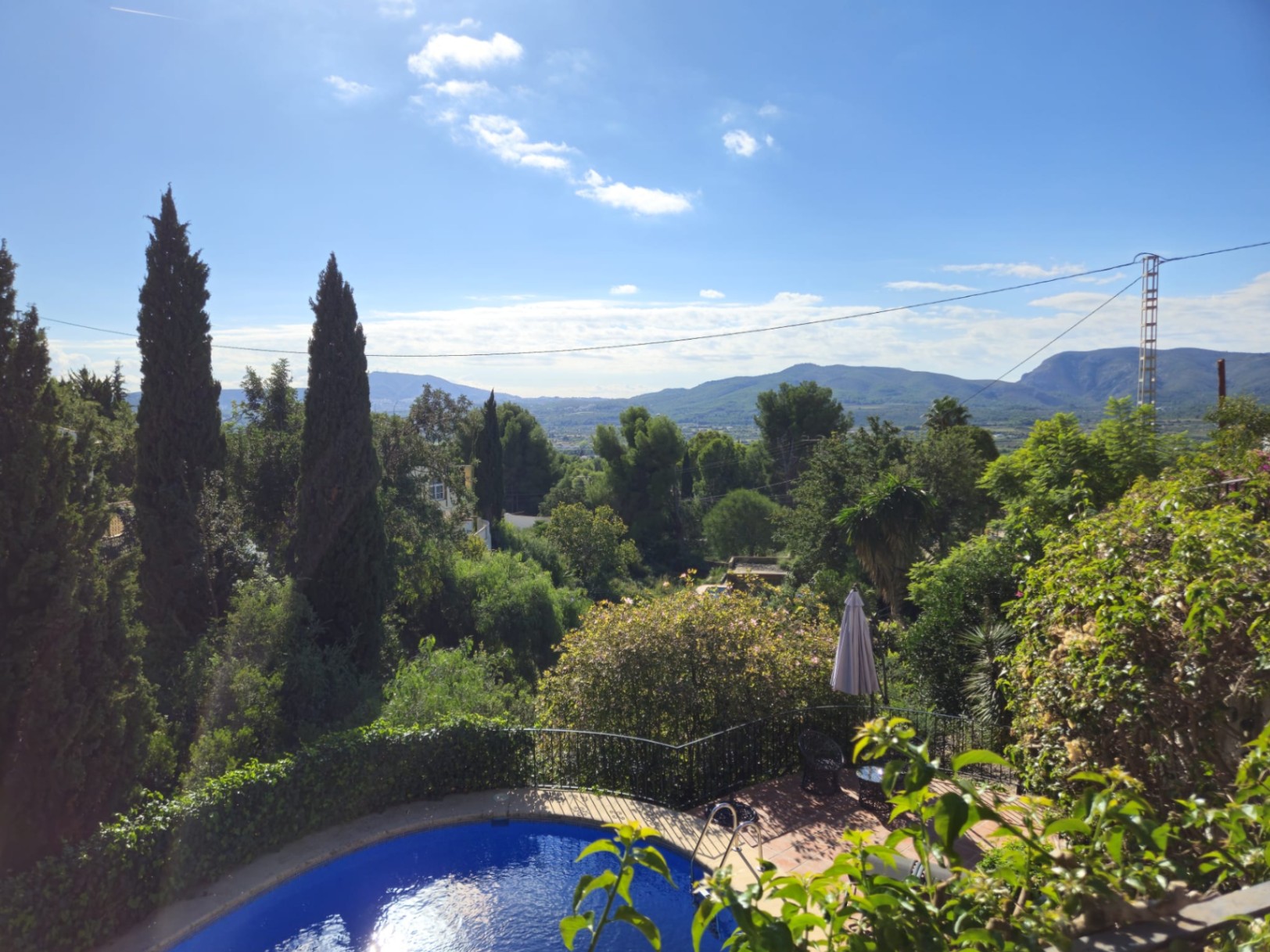 Erhöhter Blick auf einen geschwungenen Pool und eine Terrakotta-Terrasse, umgeben von Zypressen mit Panoramablick auf das Tal und die Berge.