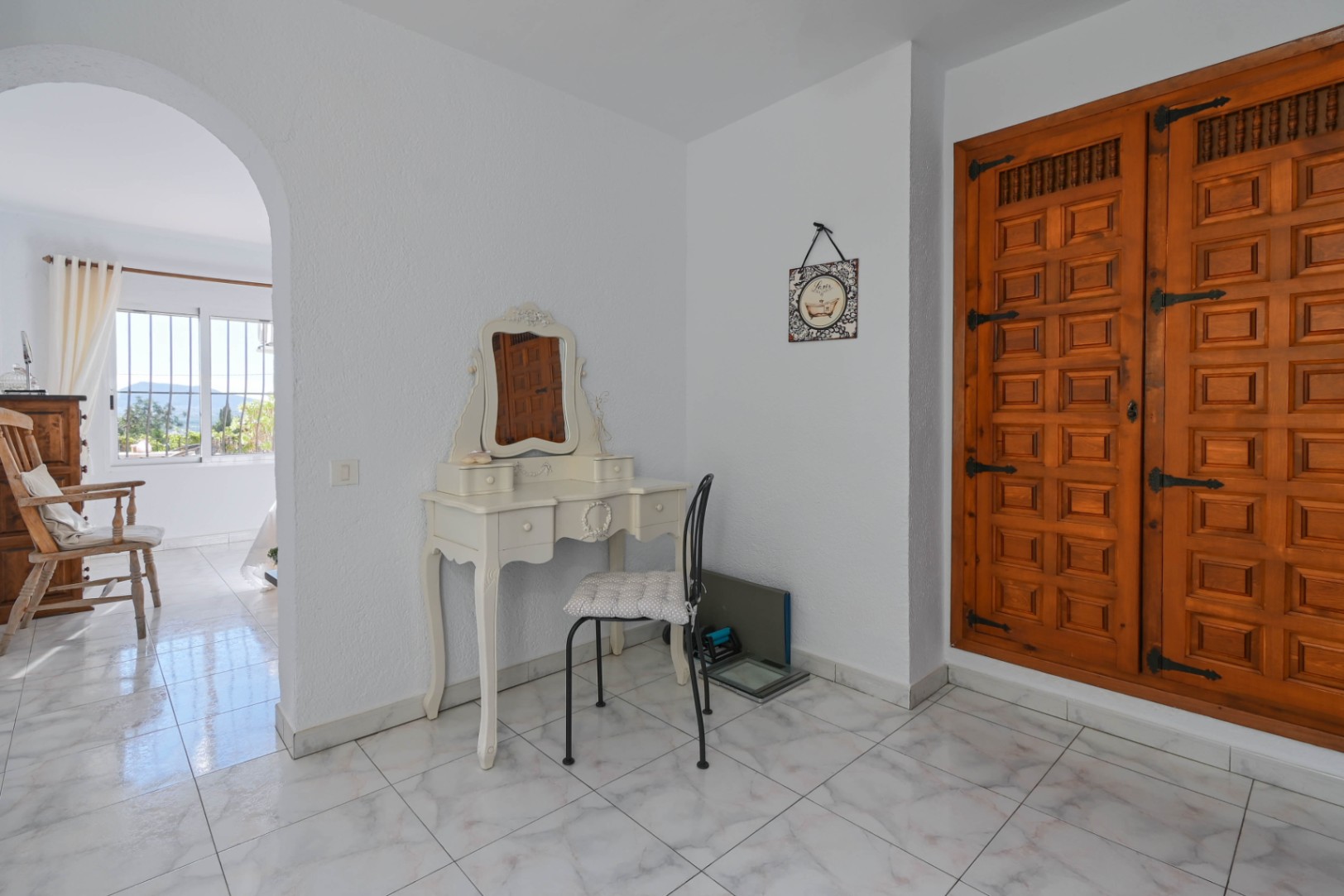 Frisierbereich mit weißem Schminktisch im Vintage-Stil und einem großen Einbauschrank aus geschnitztem Holz mit traditionellen Eisenbeschlägen.