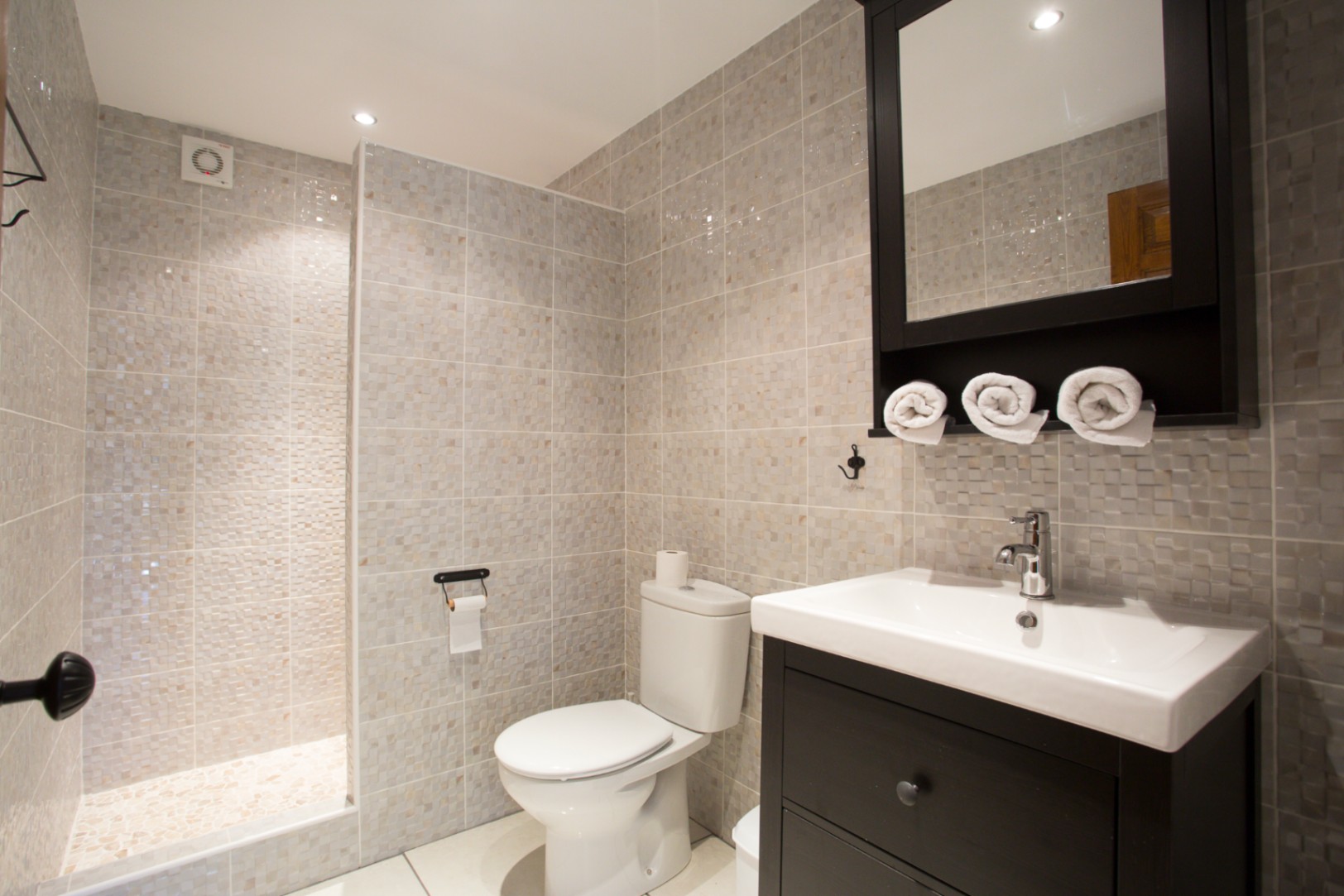 Modernes Badezimmer mit begehbarer Mosaikdusche, dunklem Waschtisch mit weißem Keramikbecken und passendem Spiegelschrank.