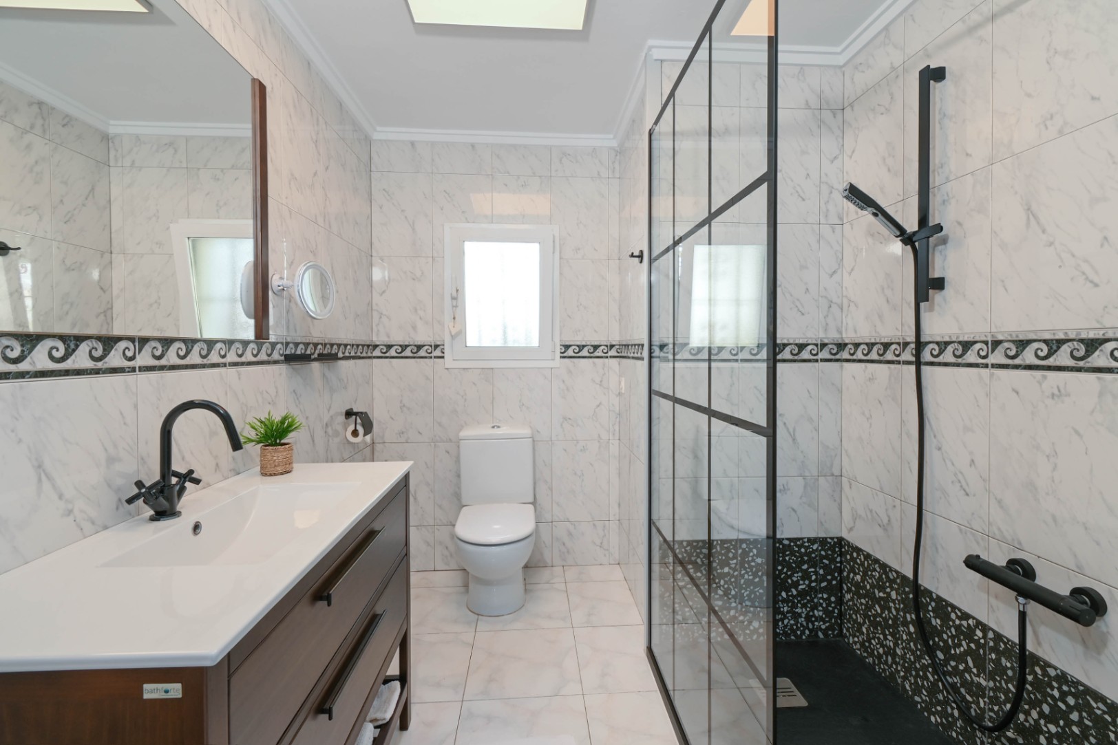 Modernes Badezimmer mit Marmoroptik-Fliesen, dunklem Holzwaschtisch und einer begehbaren Dusche mit schwarzer Glasabtrennung im Industriedesign.