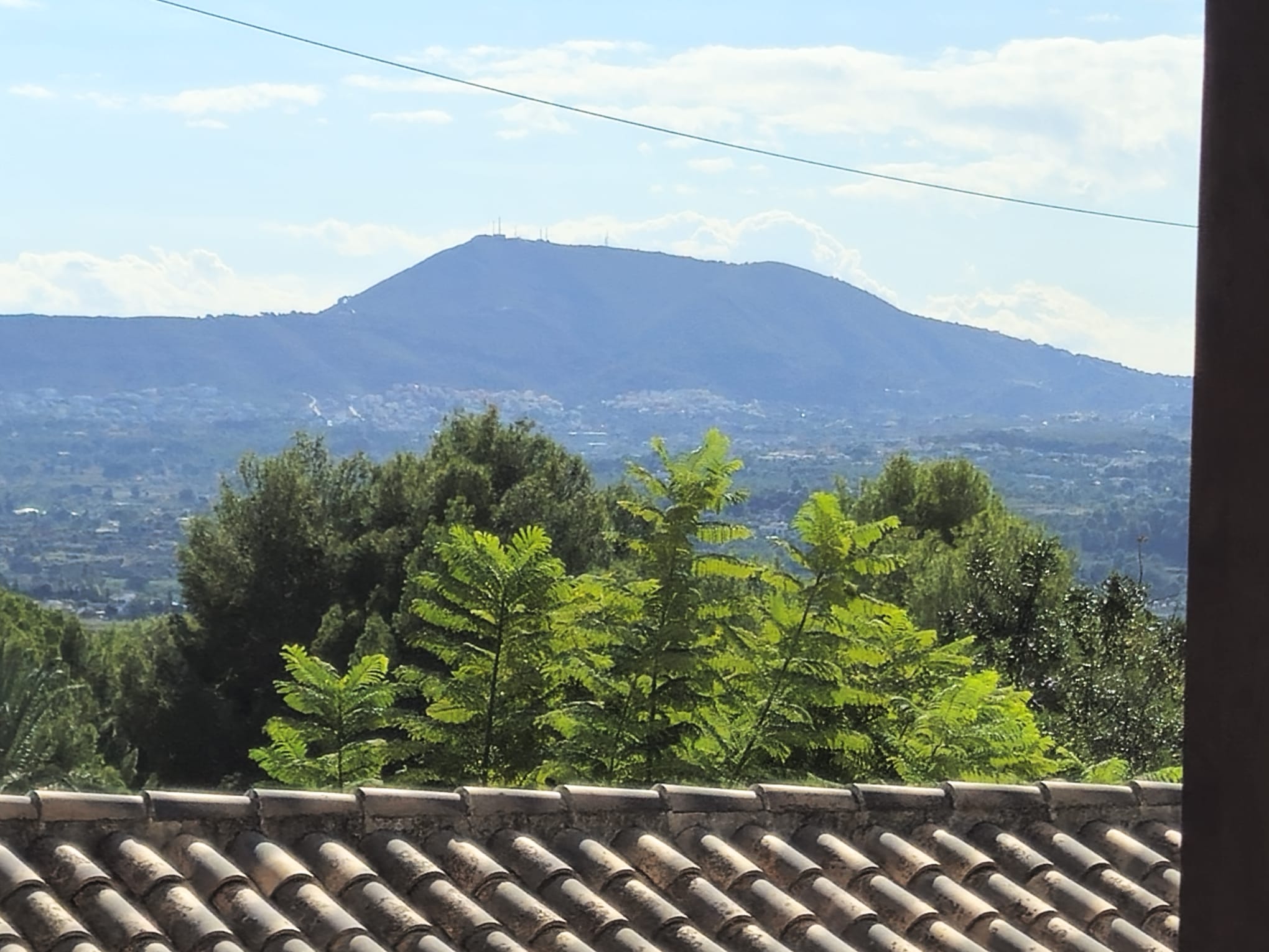 Panoramablick vom Dach mit traditionellen Tonziegeln, üppigem Grün und einem markanten Berg am Horizont unter klarem Himmel.