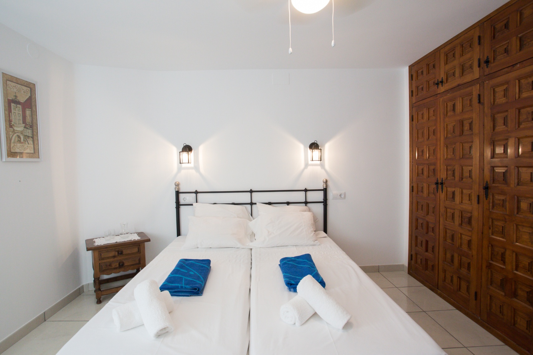 Schlafzimmer mit zwei Einzelbetten, schwarzem Eisenkopfteil, Wandlaternen und einem großen Einbauschrank aus Holz mit traditionellen Schnitzereien.