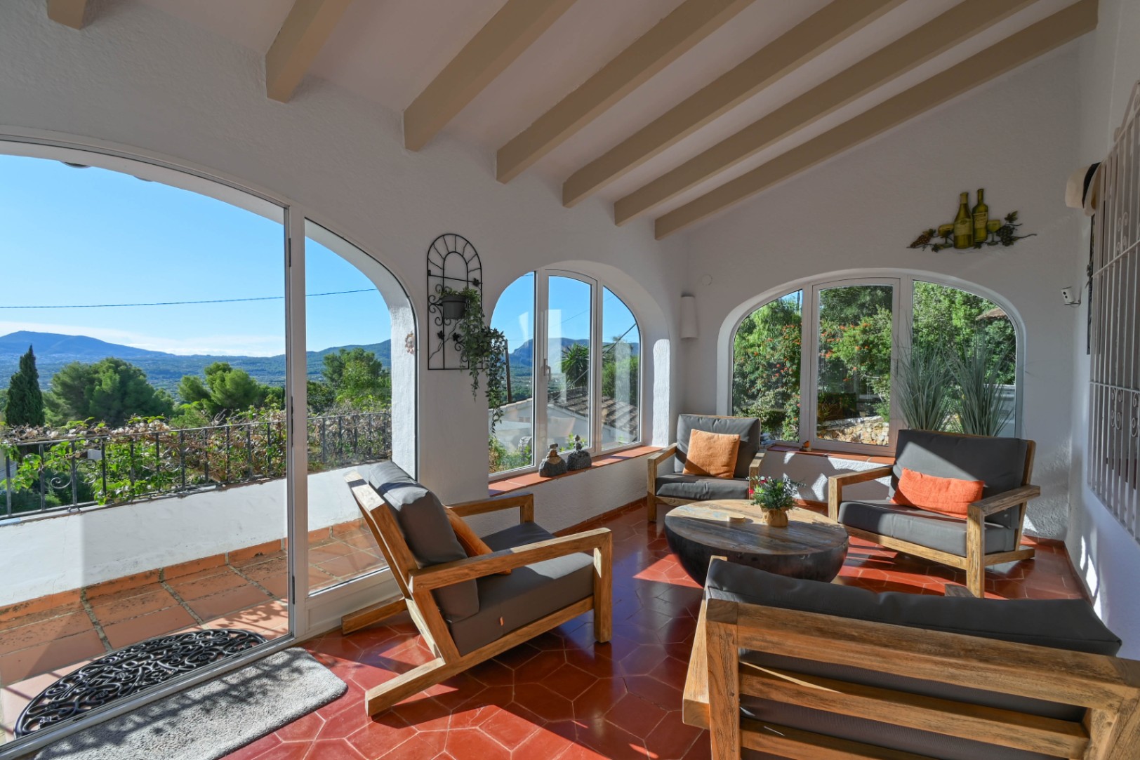 Überdachte Terrasse mit sichtbaren Holzbalken, hexagonalen Terrakotta-Fliesen und Rundbogenfenstern mit Panoramablick auf die Berglandschaft.