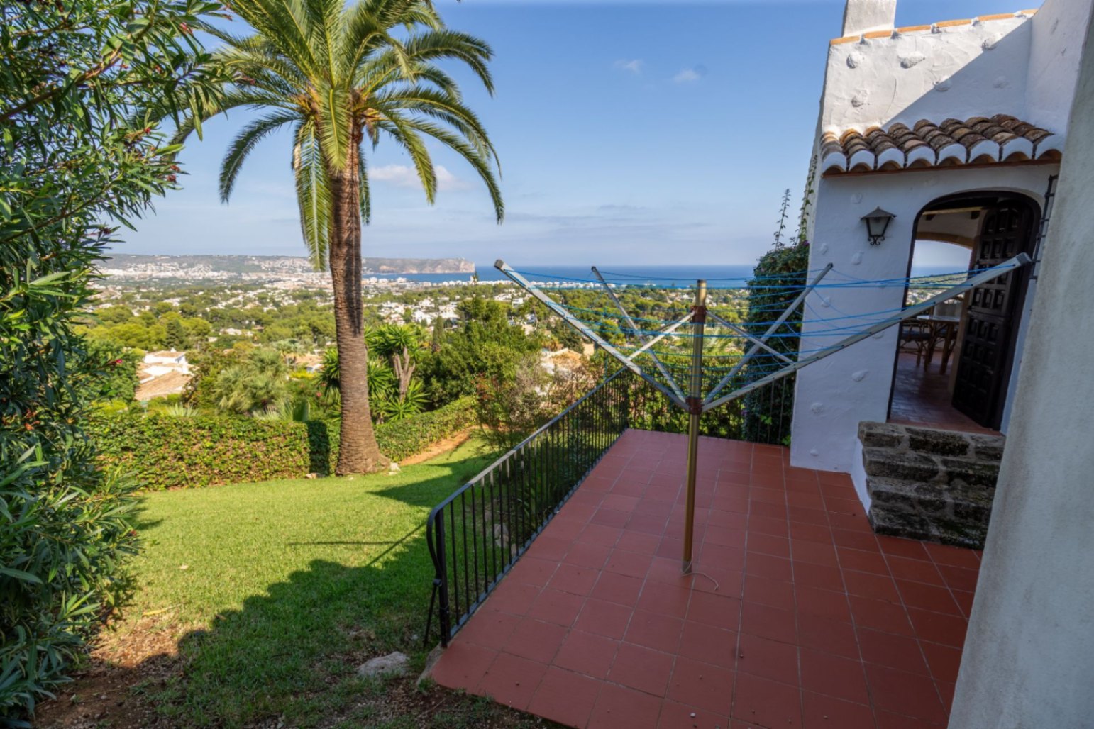 Erhöhte Terrasse mit Terrakottafliesen und Panoramablick auf das Meer und das Küstental, angrenzend an einen gepflegten Garten mit einer großen Palme.
