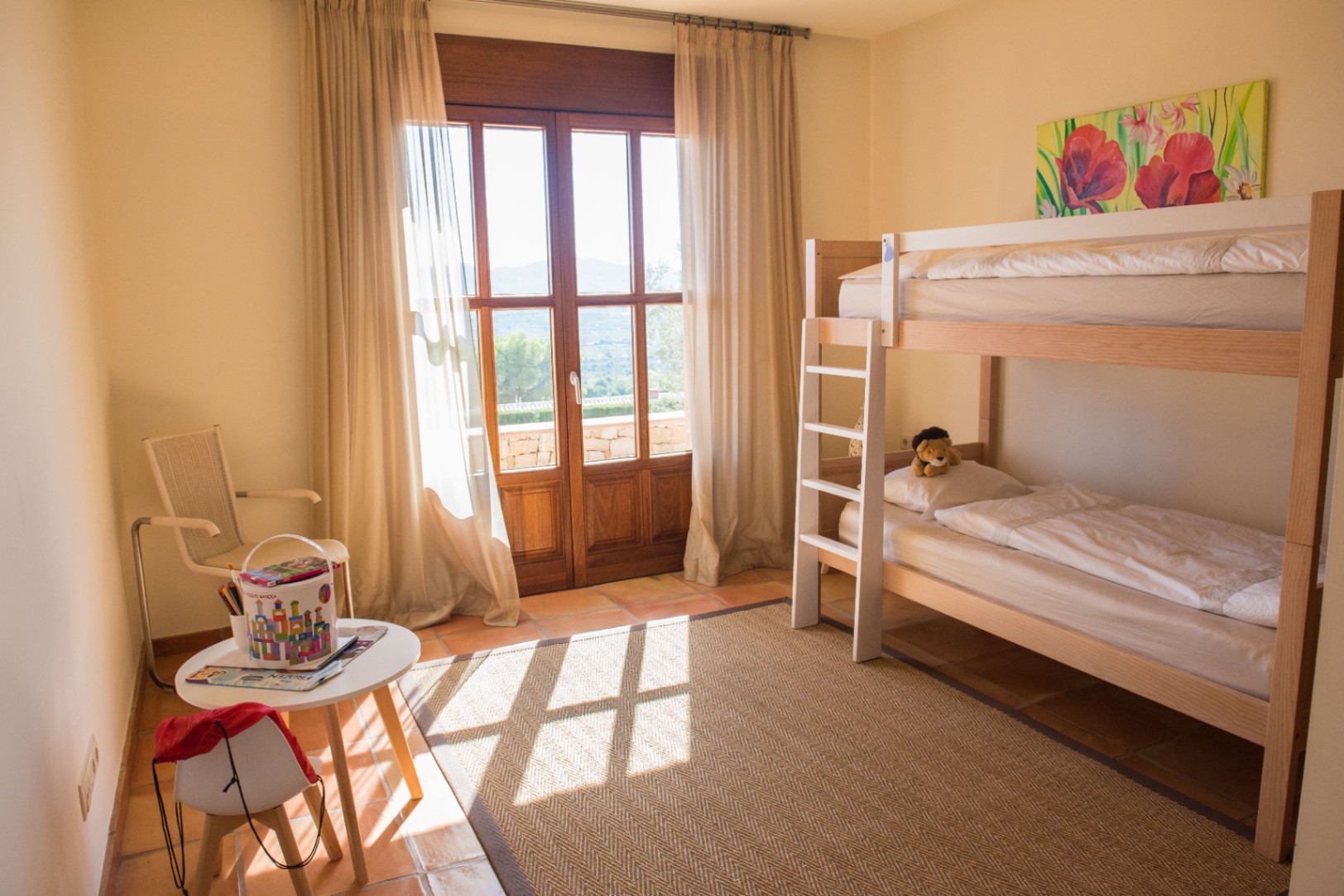Kinderzimmer mit Holz-Etagenbett, Terrakotta-Fliesen und einer großen Glastür, die auf eine Terrasse mit Blick auf die umliegende Landschaft führt.