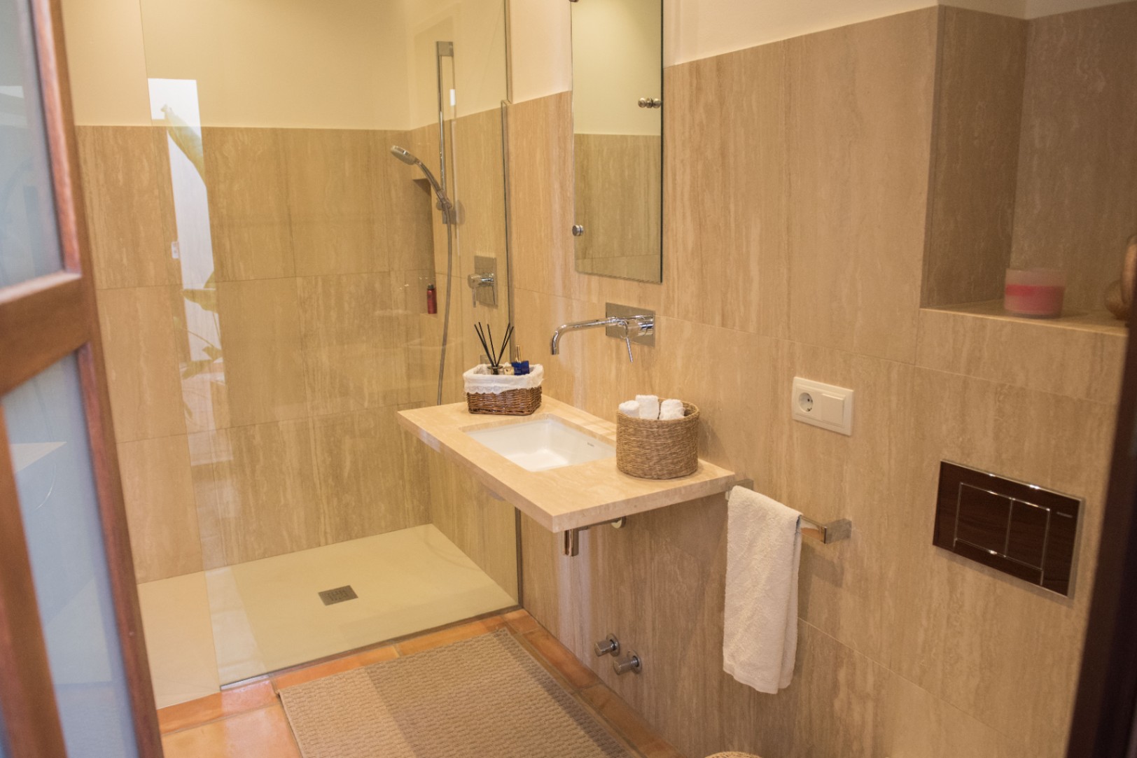 Modernes Badezimmer mit begehbarer Dusche, schwebendem Waschtisch aus Naturstein und Unterputz-Armaturen vor beigefarbenen Travertin-Fliesen.